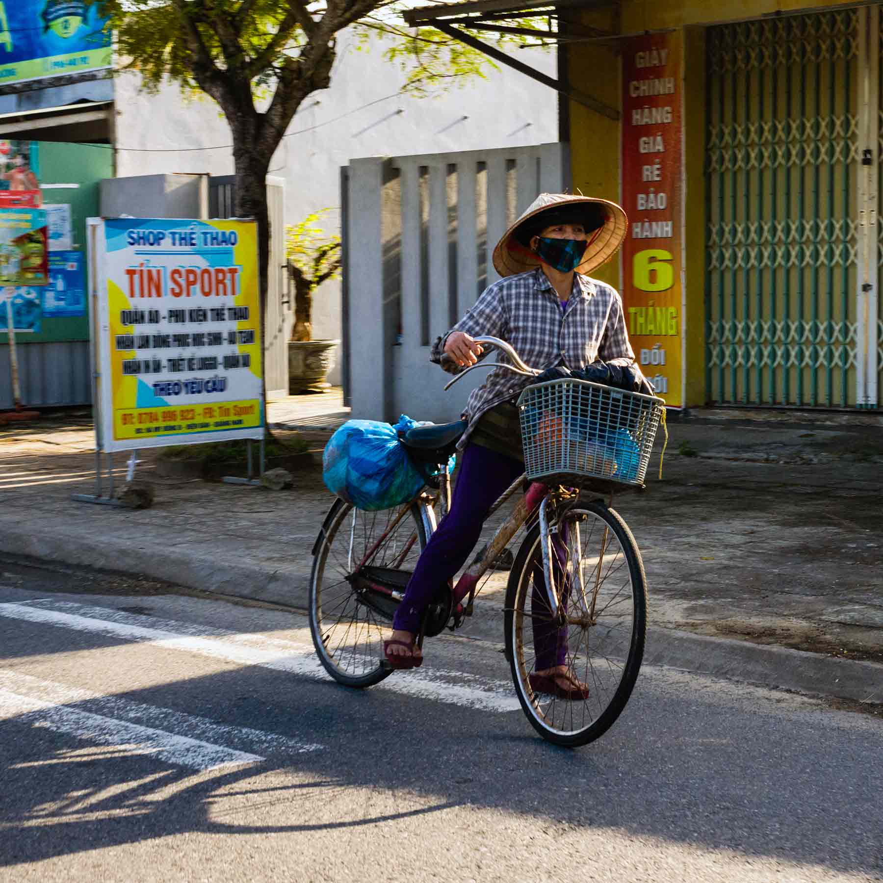 Vietnamese cyclist in traditional attire and face mask navigating a quiet urban street.