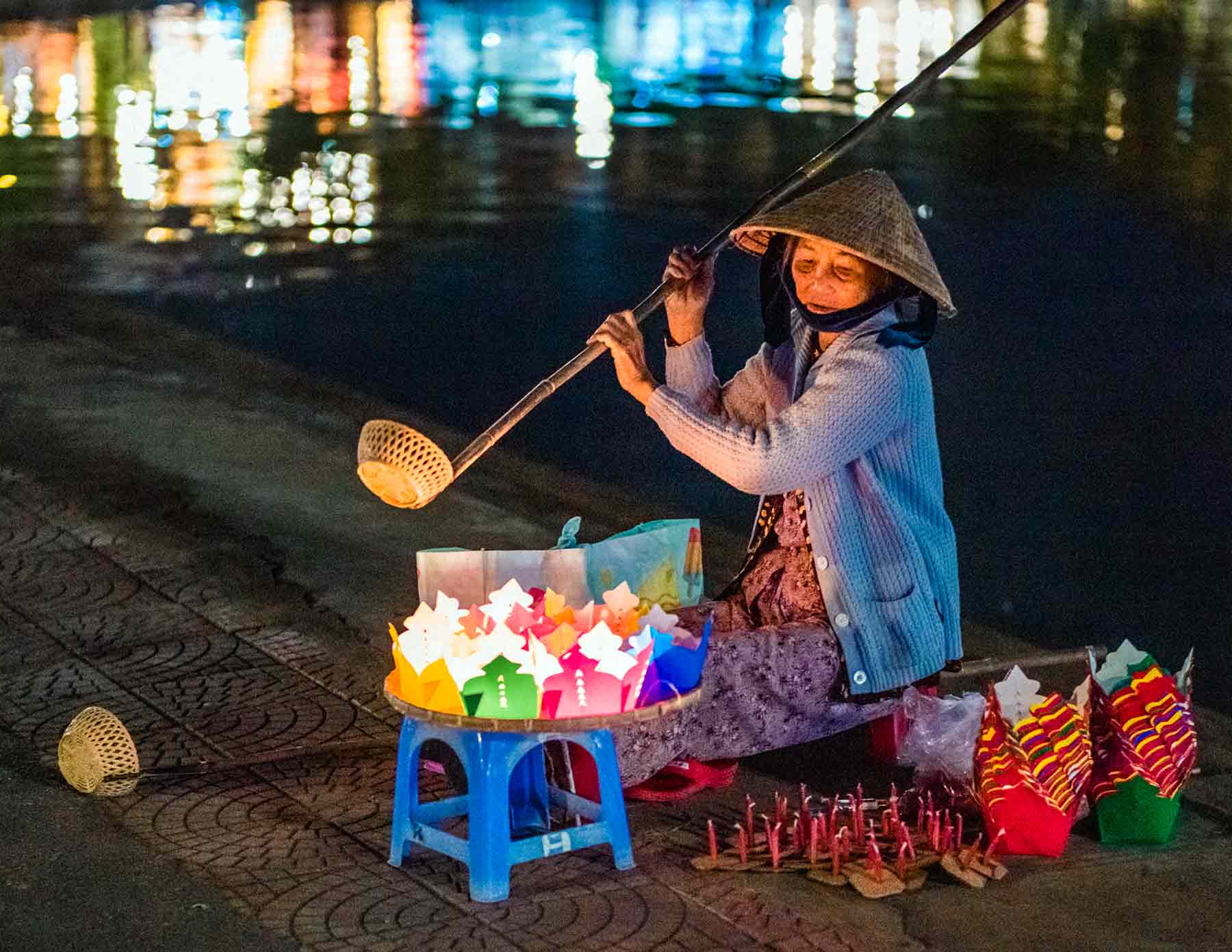 A Hoi An Vietnamese vendor selling colorful lanterns by a reflective river at night.