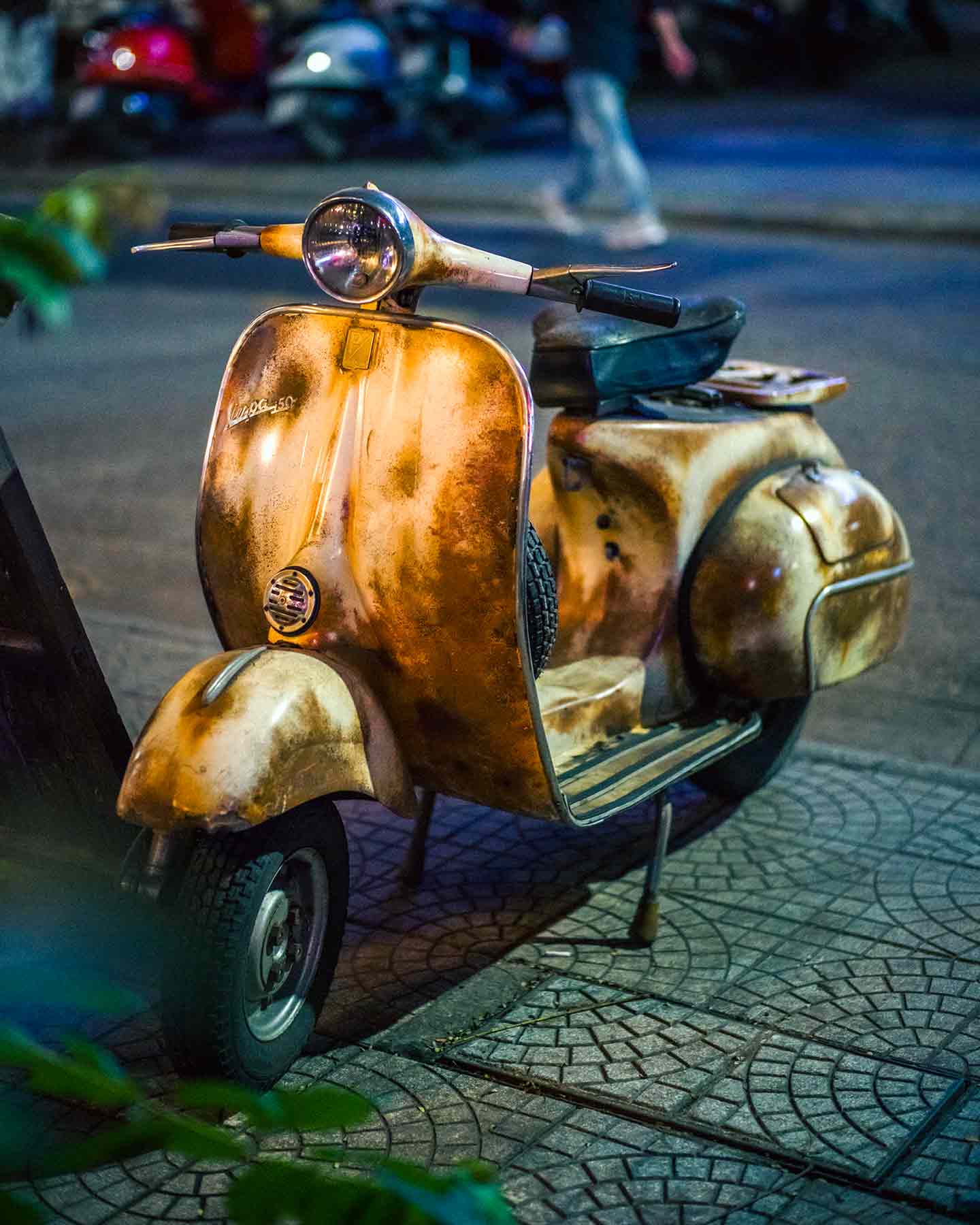Vintage, rusted Vespa scooter parked in vibrant city night scene, embodying urban resilience and history.