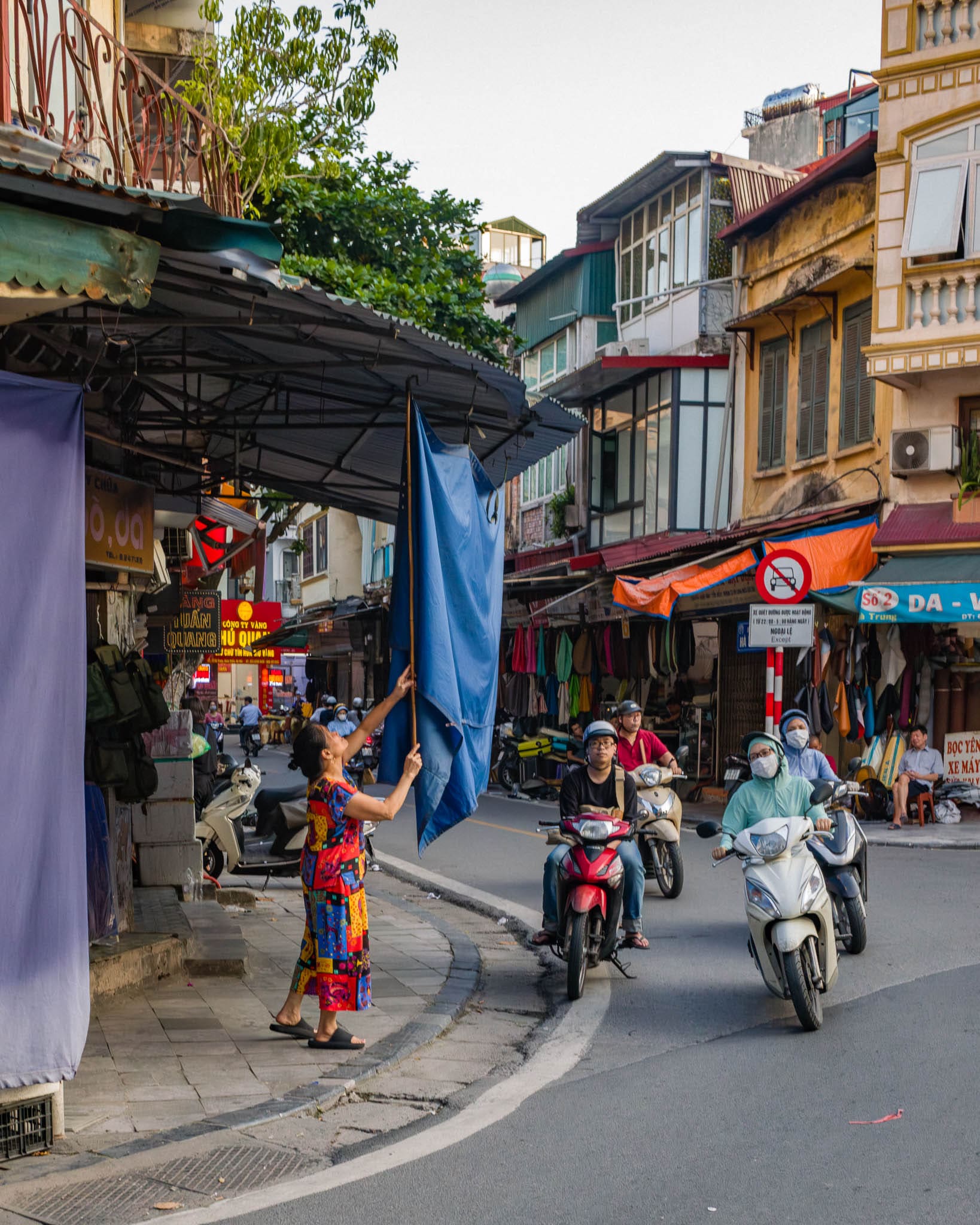 Bustling Hanoi city street with traditional buildings, motorbikes, and vibrant local life.