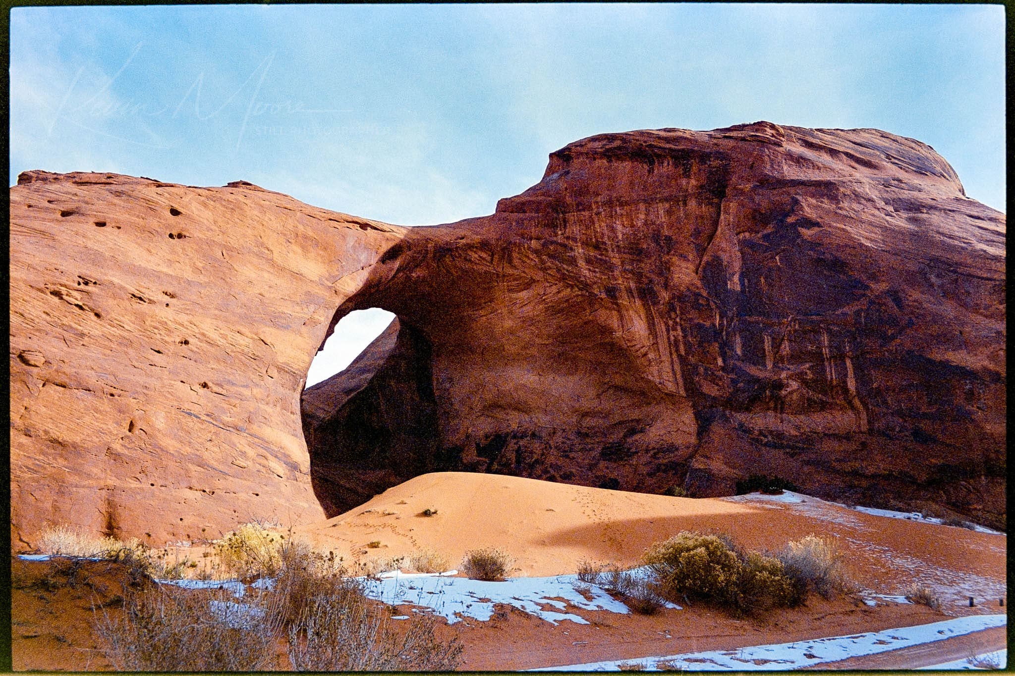 Stunning sandstone arch formation in a desert landscape with patches of snow.