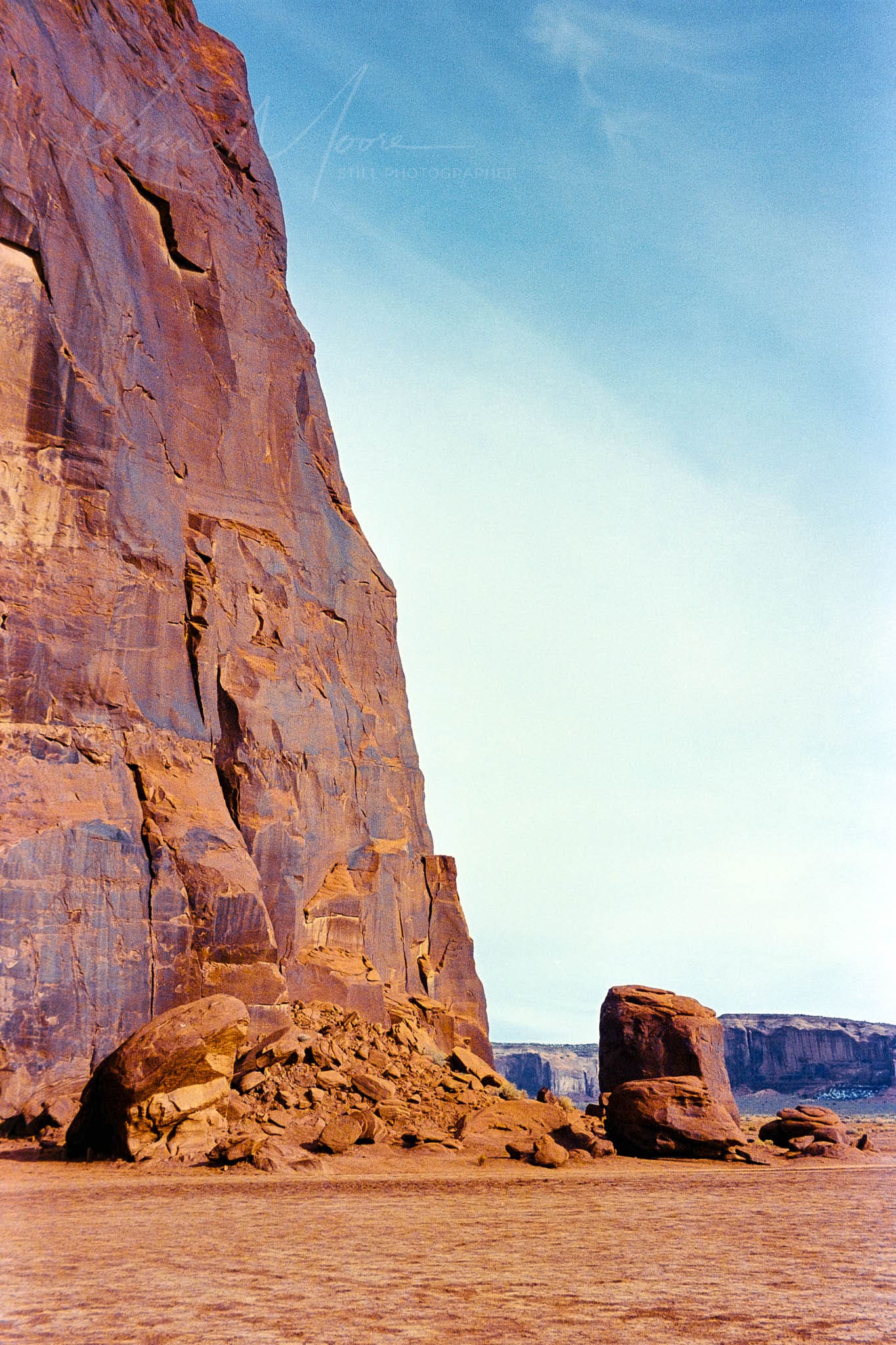 Stunning desert landscape featuring a massive reddish-brown cliff under a clear blue sky.