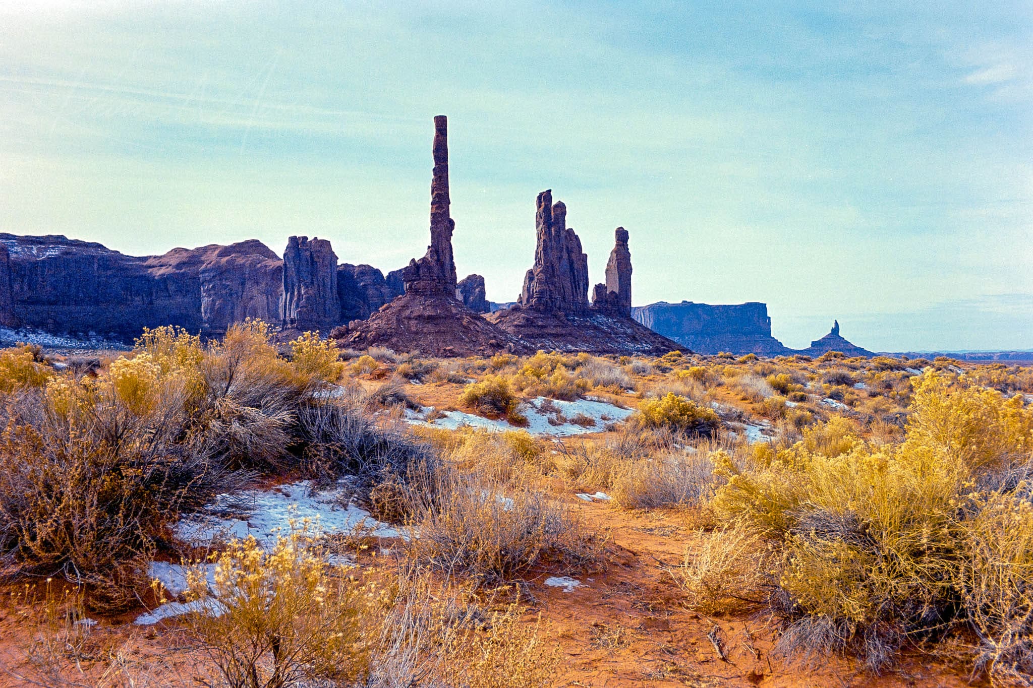 Dramatic desert scene with towering buttes and vibrant vegetation under a clear blue sky.