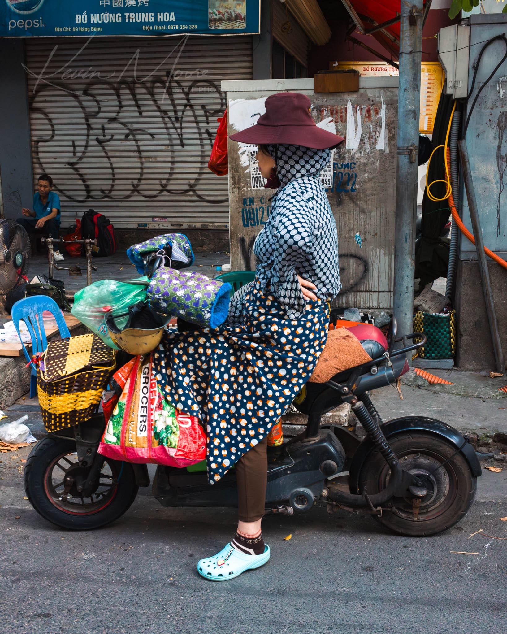 Woman transporting goods on a scooter in a vibrant urban Hanoi setting.