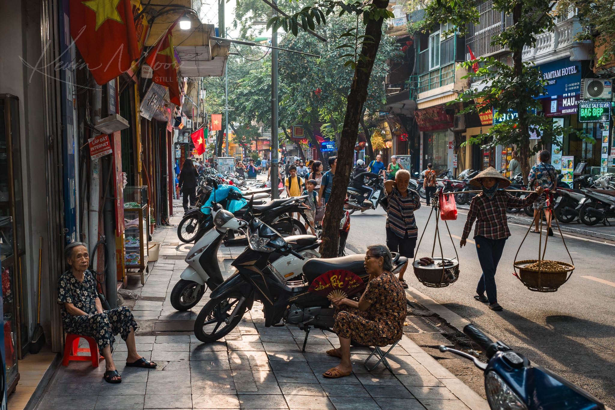 Bustling Hanoi street with motorbikes, pedestrians, and traditional vendor in Vietnam.