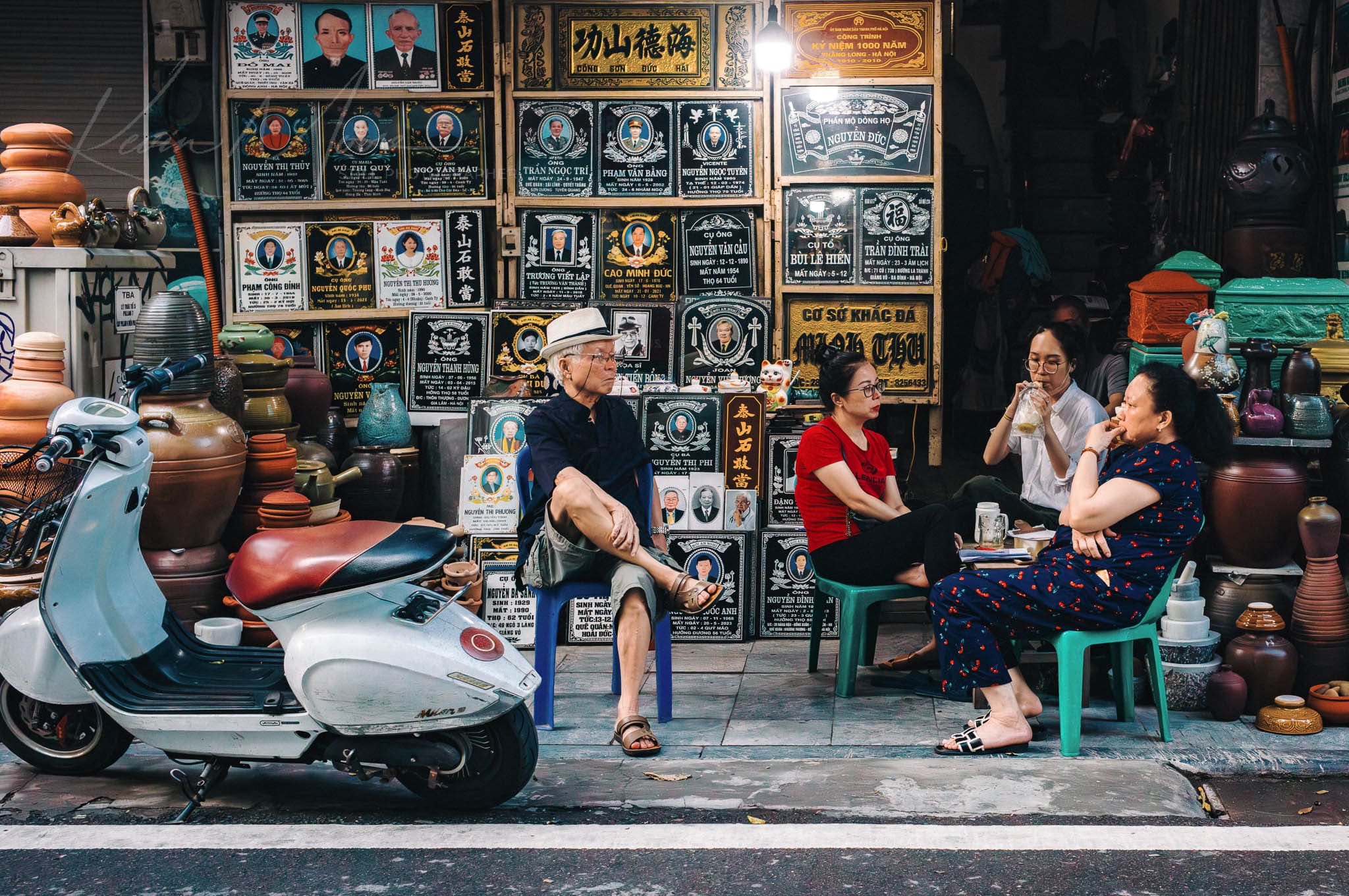 Locals socializing on vibrant Hanoi street with scooters outside of a funeral home.