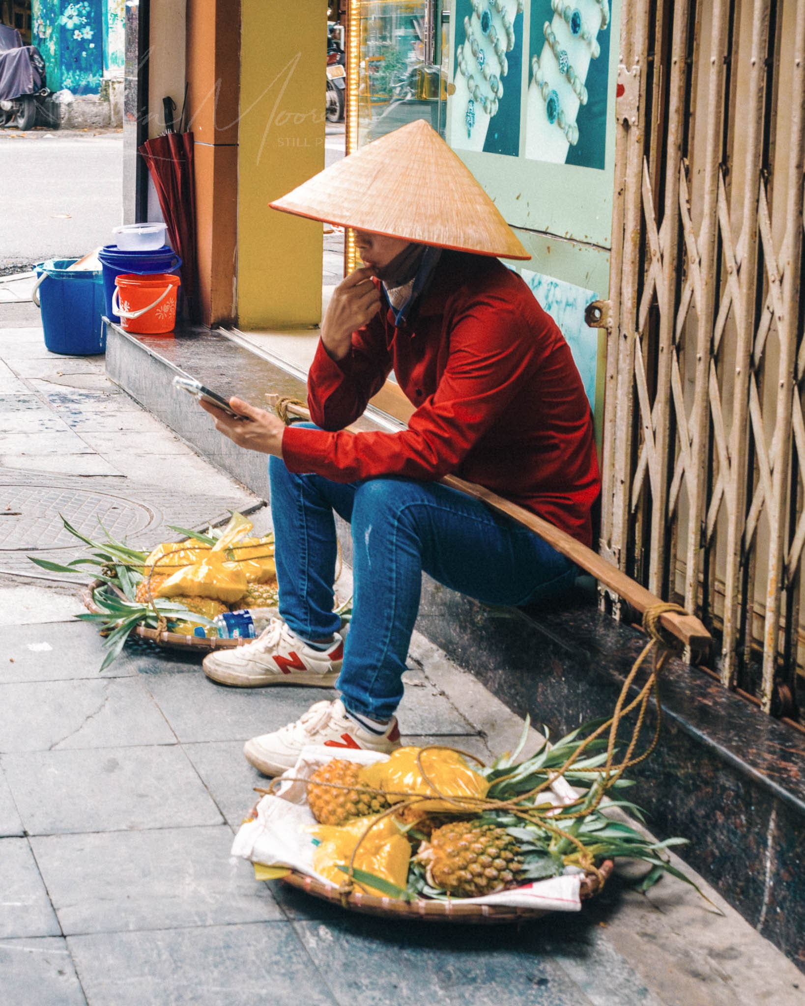 Street vendor in Hanoi Vietnam selling fresh pineapples, using smartphone during break.