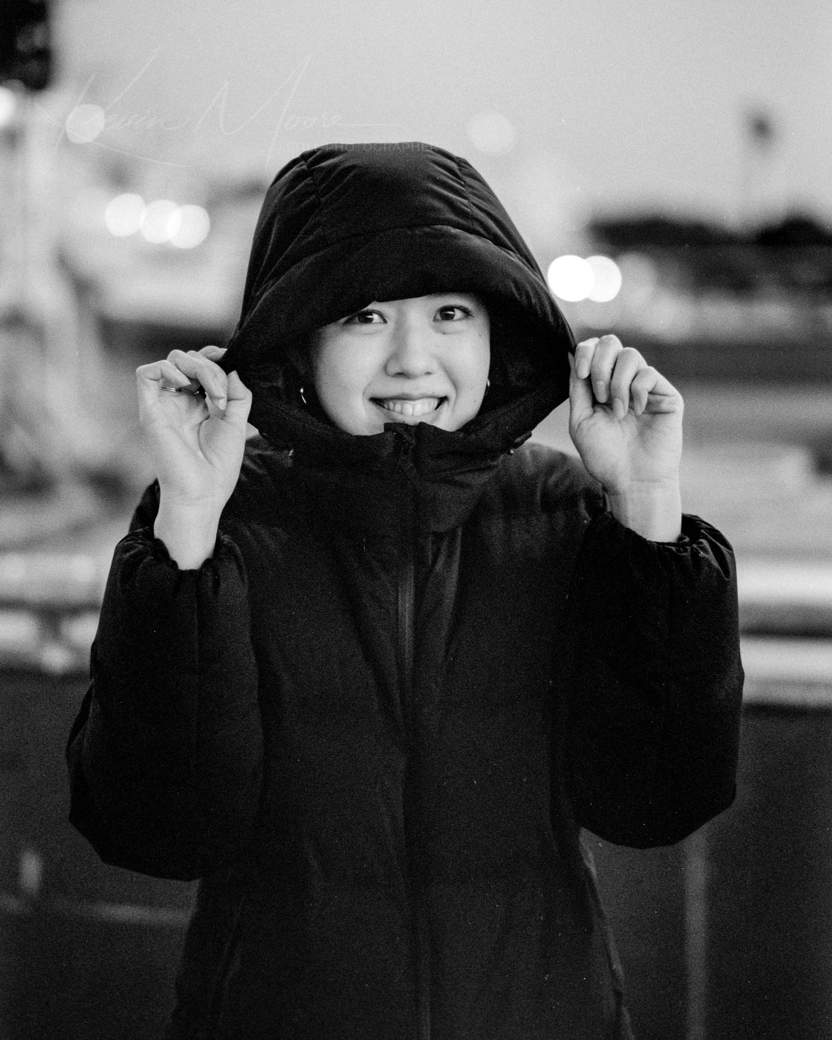 Woman with hooded jacket smiling joyfully in a night setting.