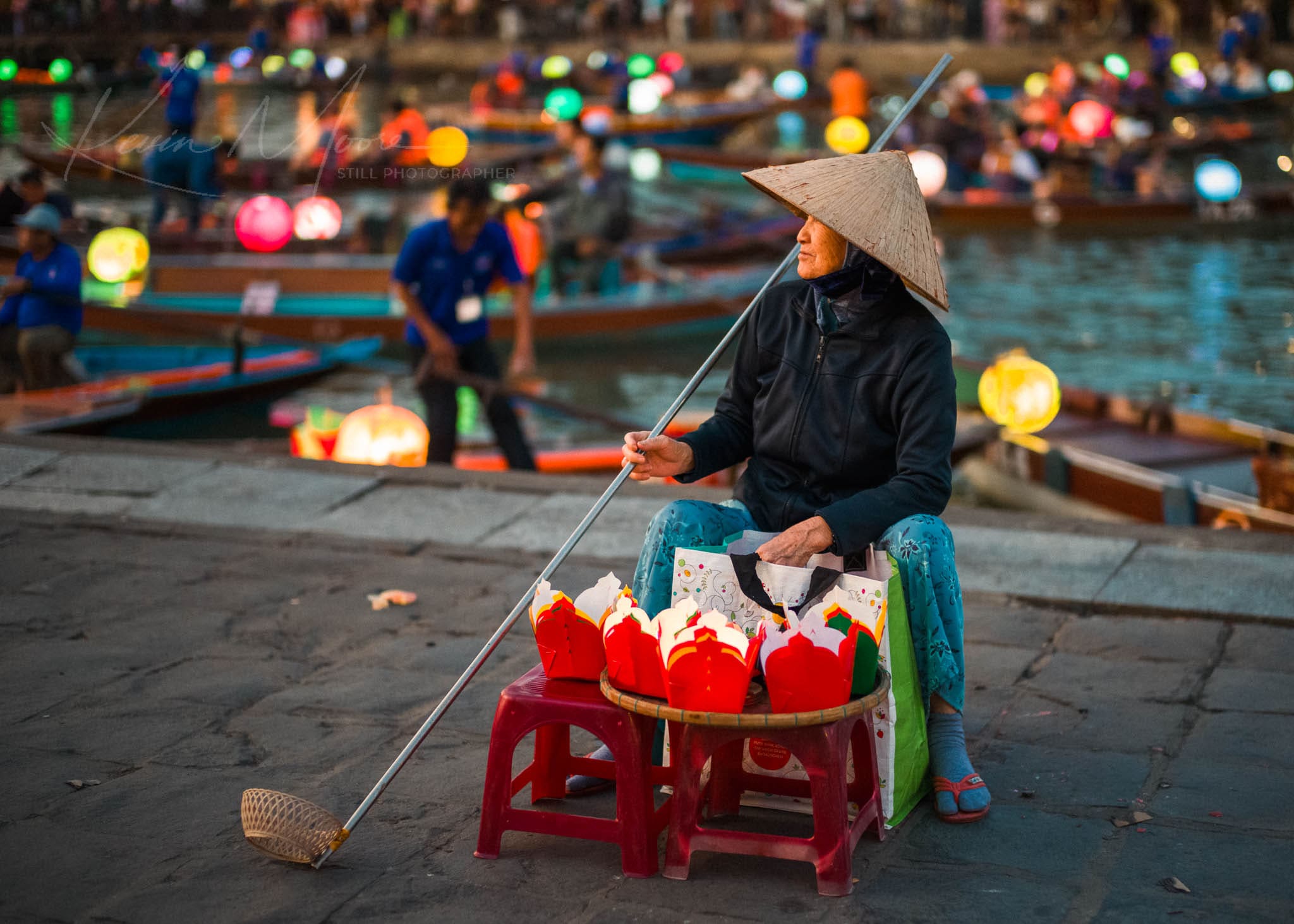 Person selling vibrant lanterns by a bustling riverside festival in Vietnam.
