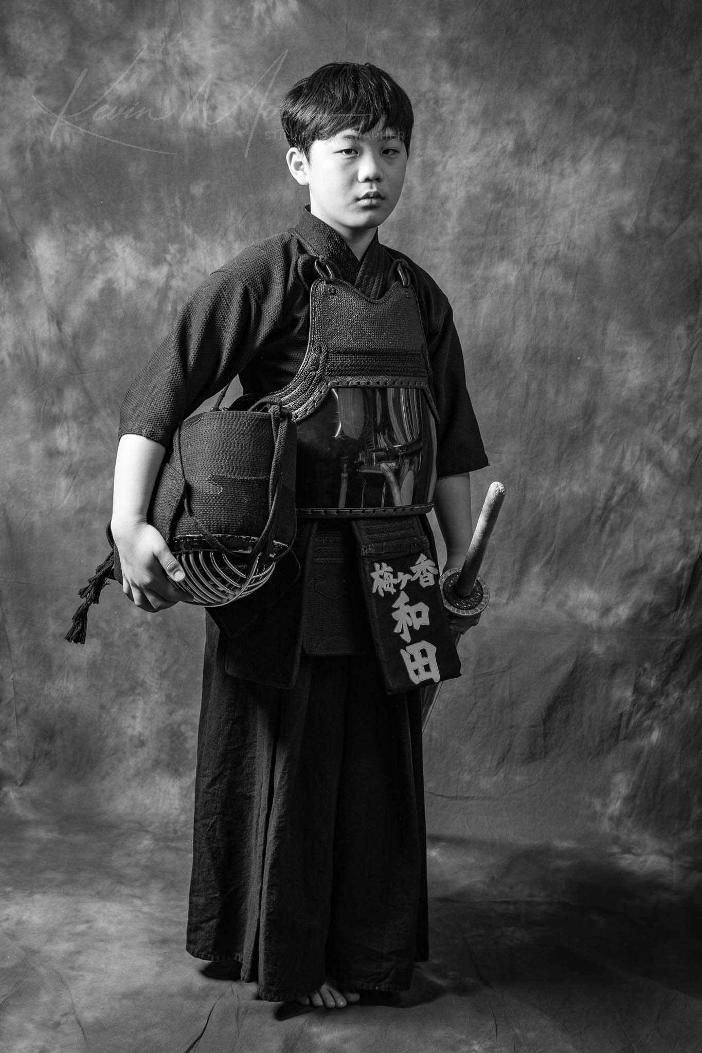 Monochrome portrait of a martial artist in traditional Japanese attire holding a sword.