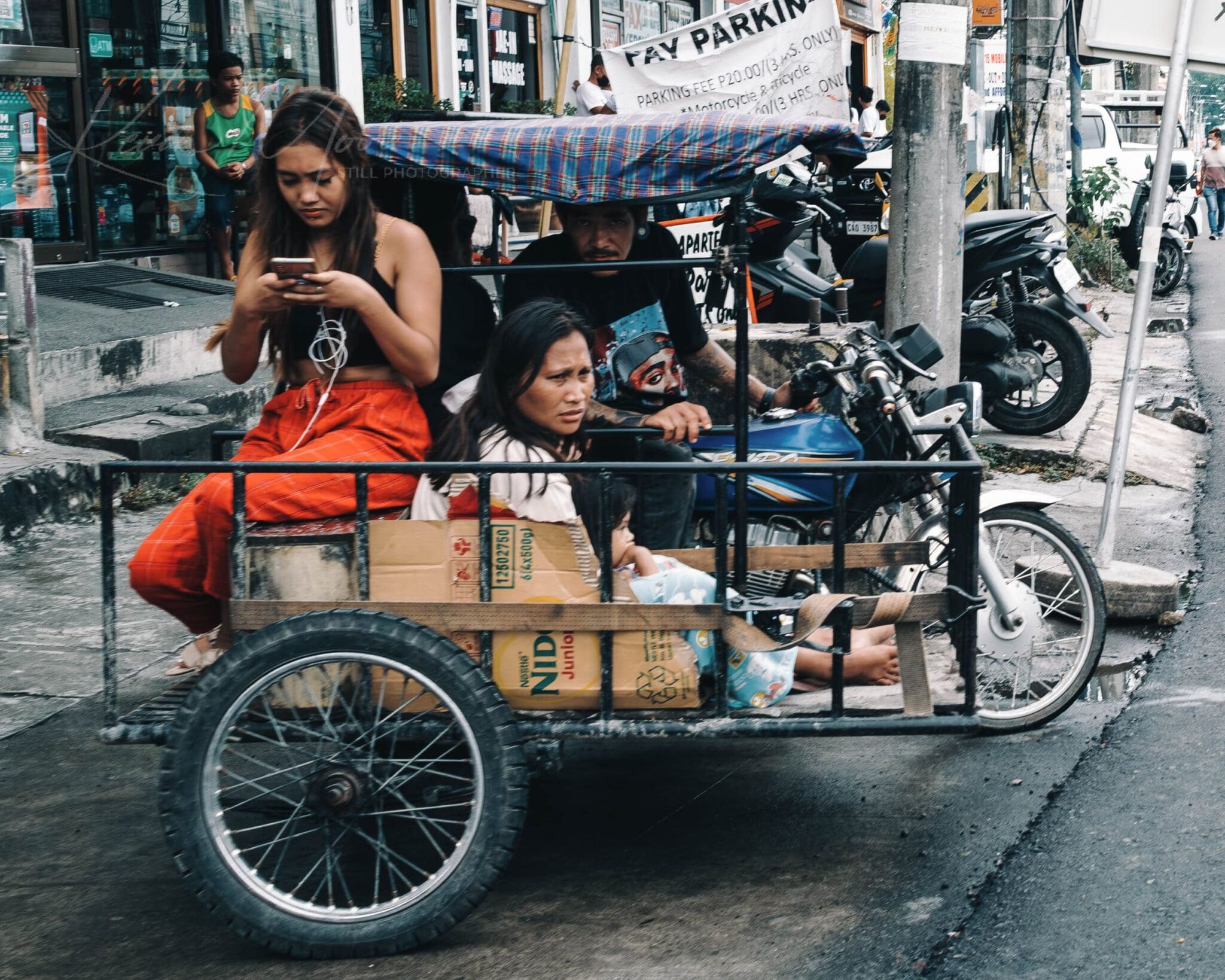 Women using smartphone in a cargo tricycle on a busy urban street after rain.
