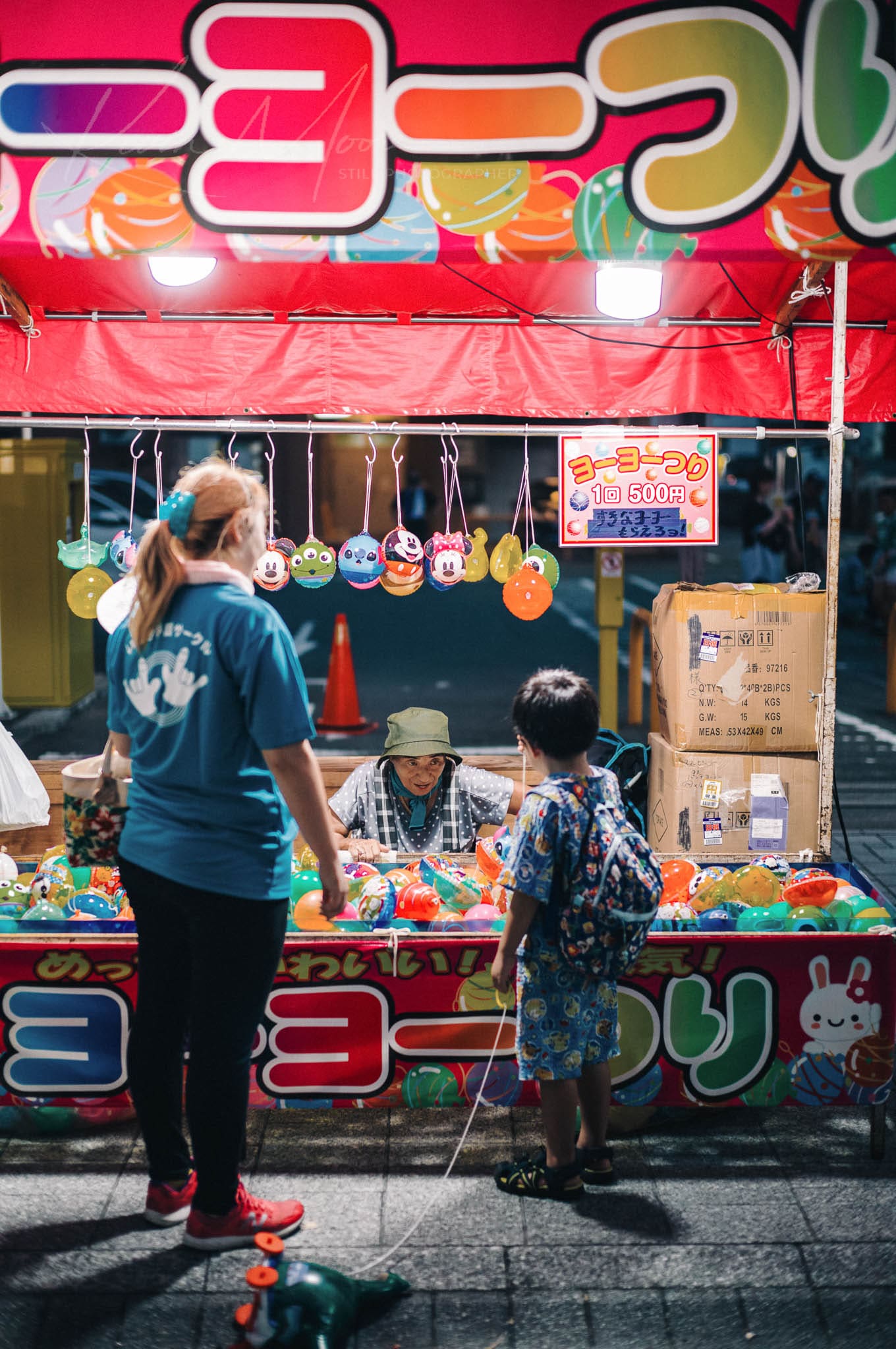 Adult and child exploring a vibrant toy stall at a bustling night festival.