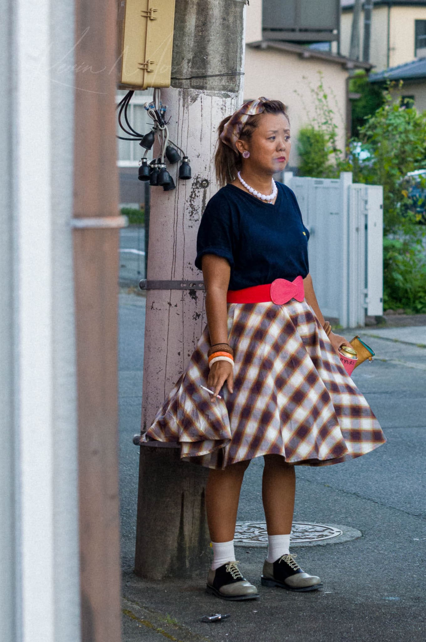 1950s-inspired street style portrait in a tranquil suburban setting, featuring plaid skirt and saddle shoes.