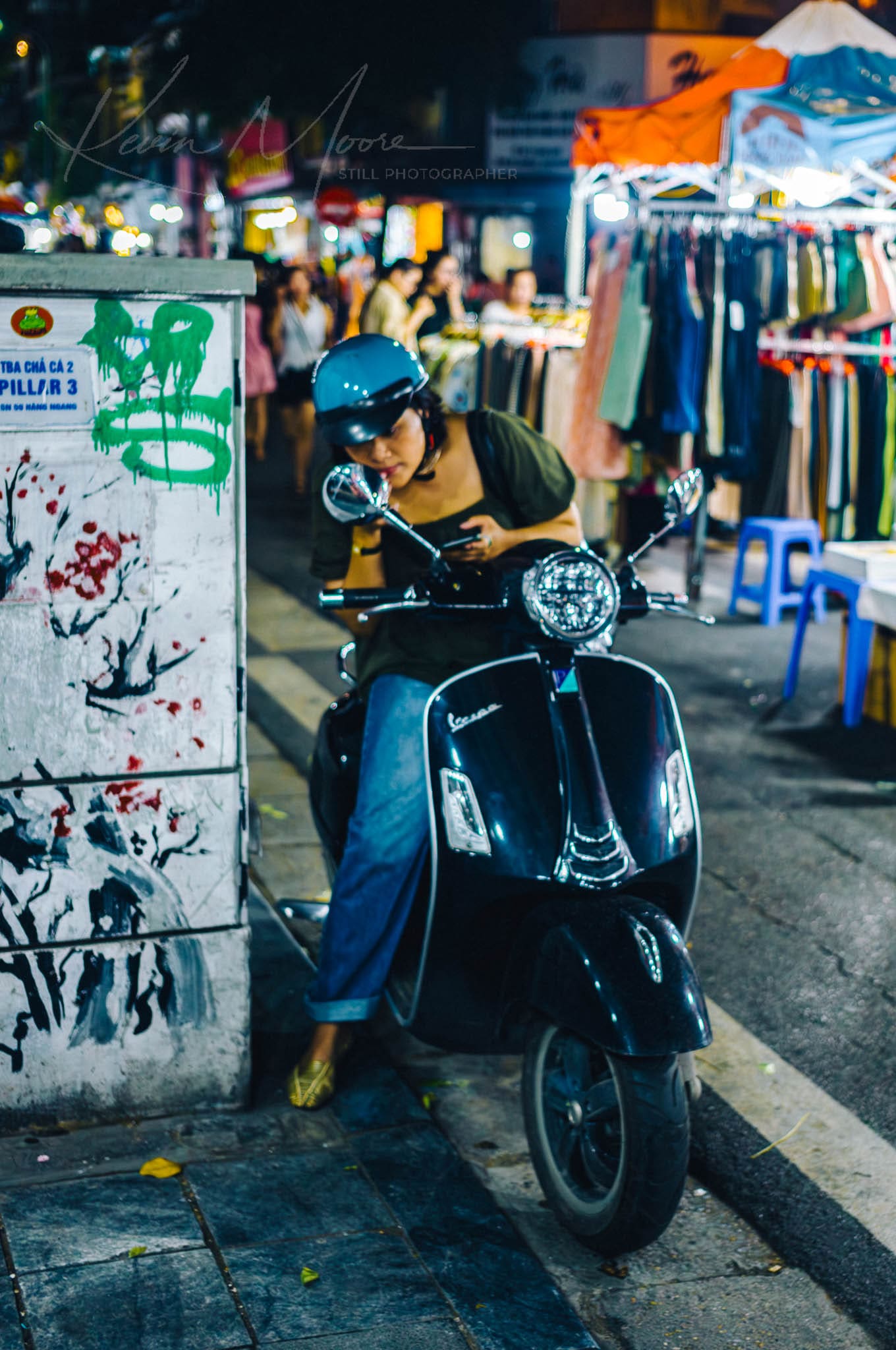 Woman applies makeup on vintage scooter at vibrant Hanoi night market.