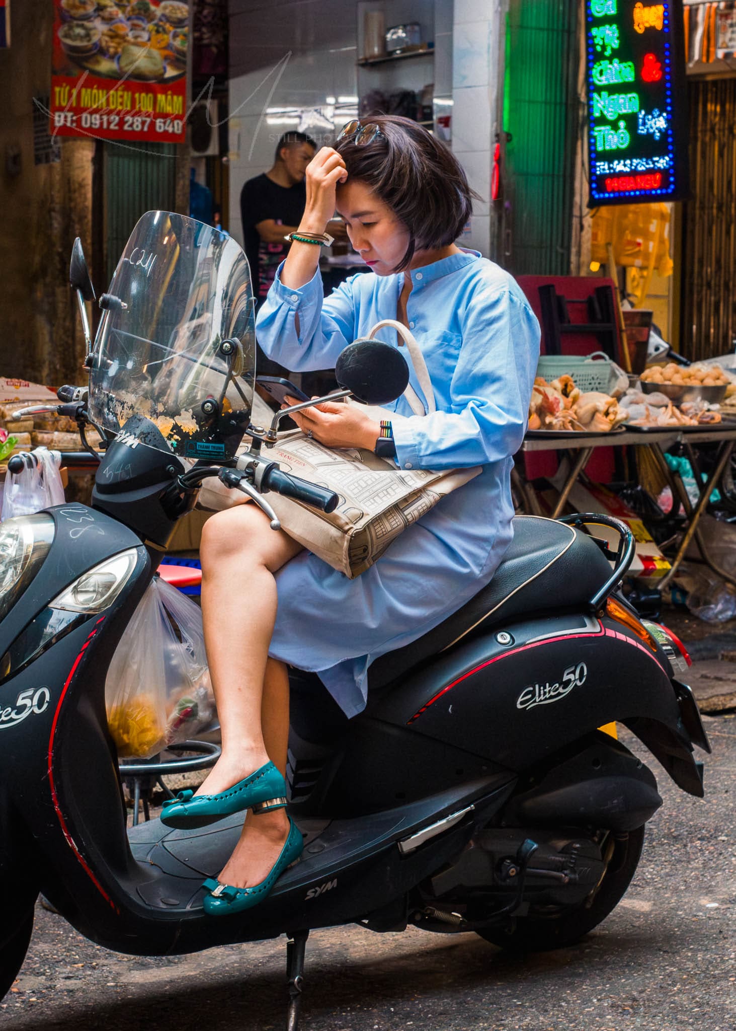 Scooter Rider Checks Her Phone in Vibrant Hanoi Market