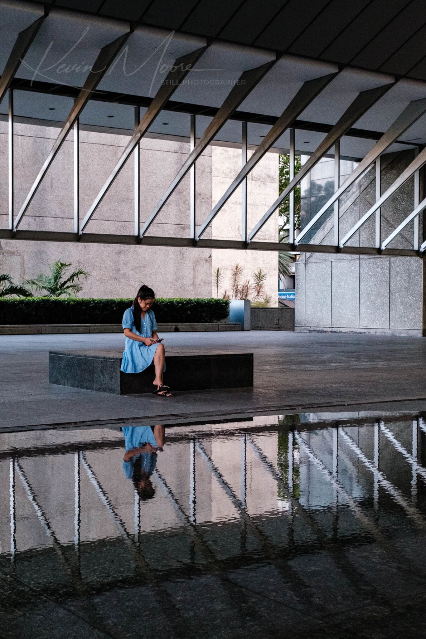 Solitary woman in modern, geometric architecture with reflections on water.