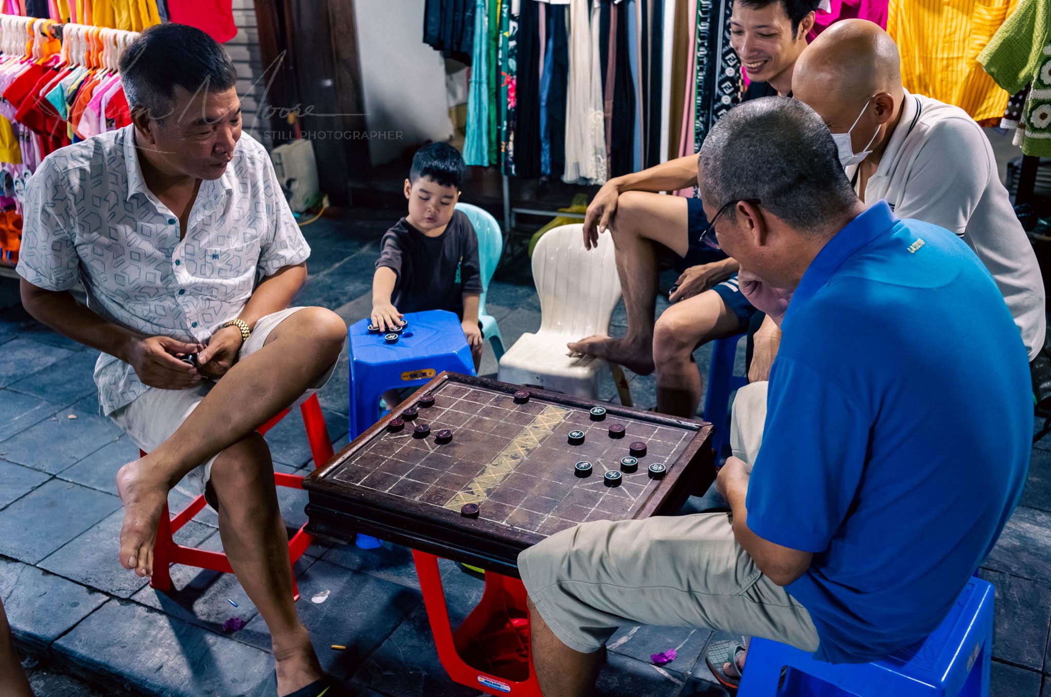 Men and a child engrossed in a Hanoi night market Chinese chess game.
