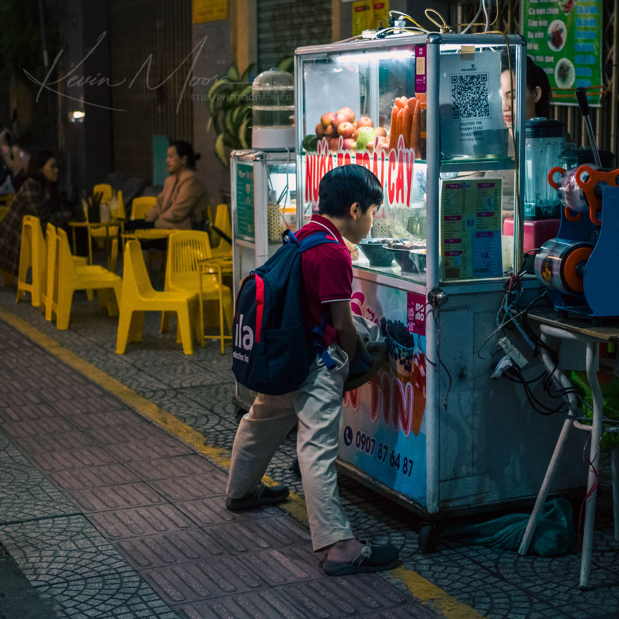 Child ordering street food from a brightly lit vendor cart at night in urban setting.