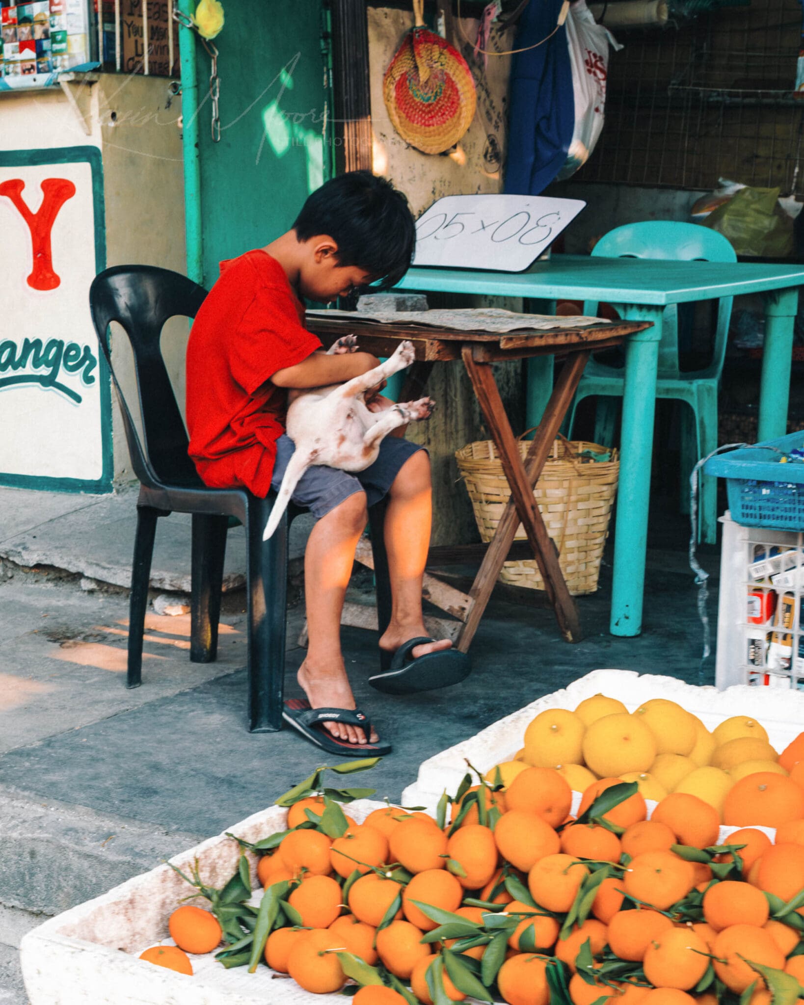 Boy engrossed in playing with puppy at vibrant street market in urban Philippines.