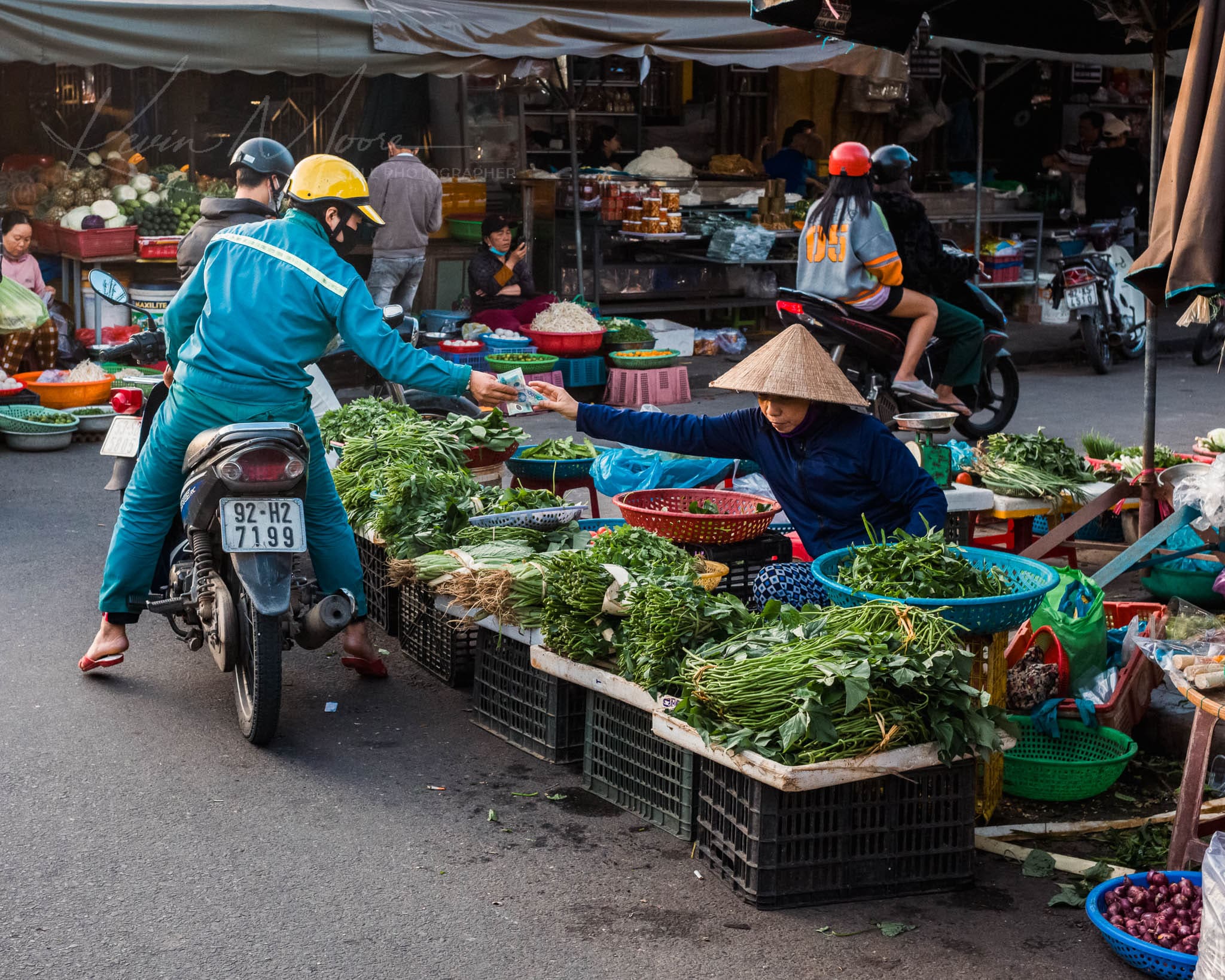 Busy Vietnam street market with fresh produce and a passing motorcyclist.
