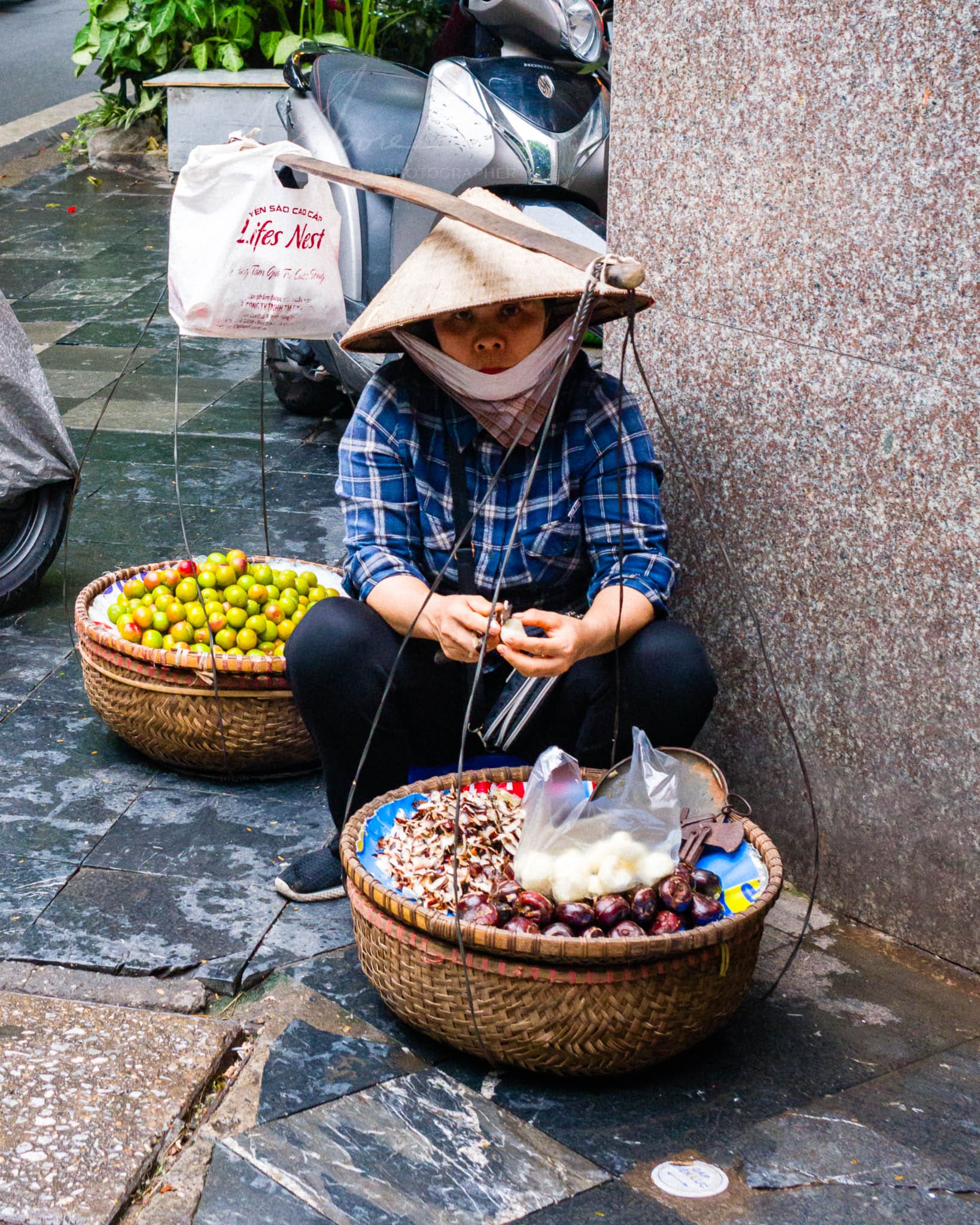 Hanoi street vendor selling fresh fruit and nuts under a traditional hat.