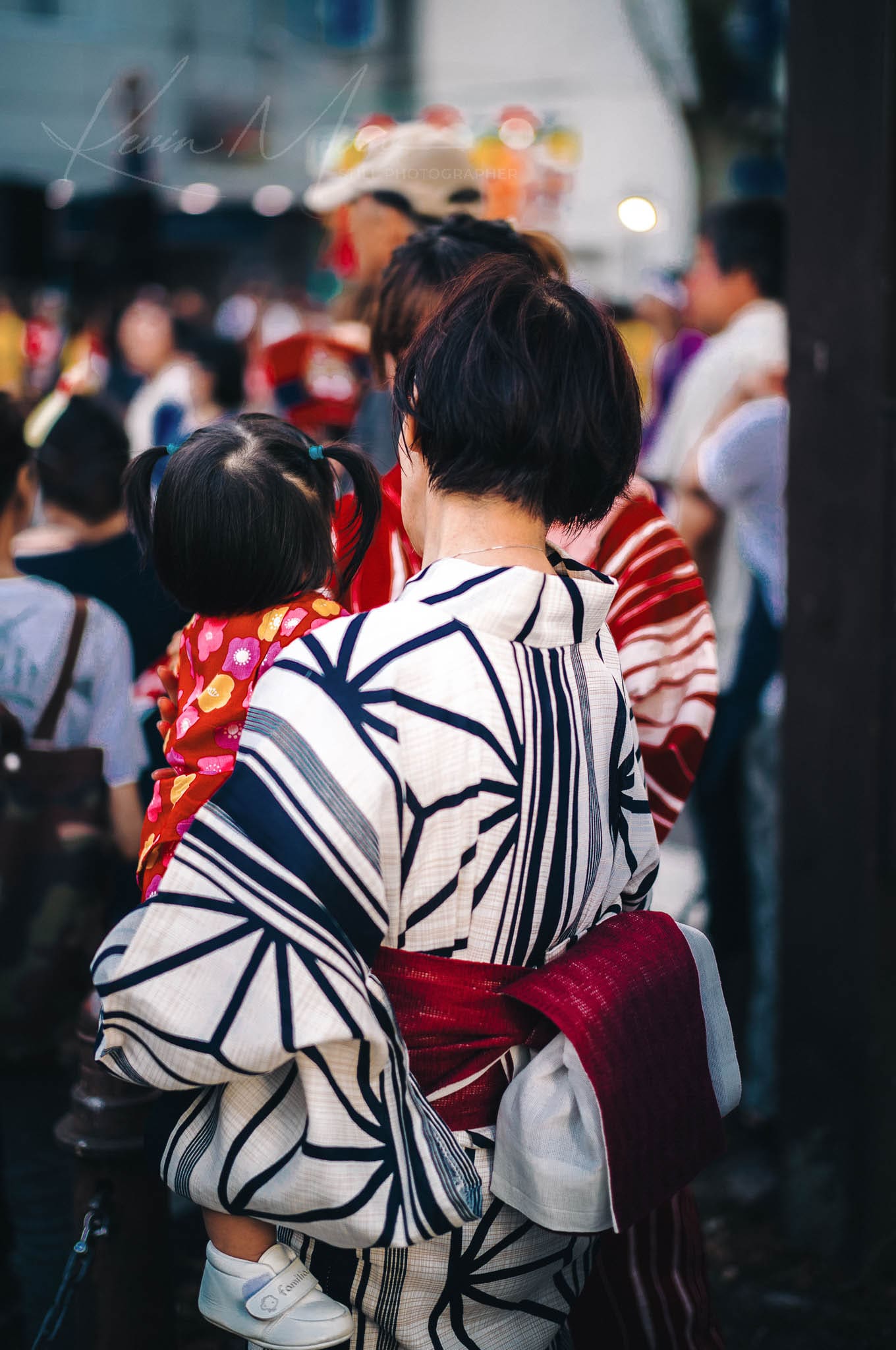 Adult and child in traditional attire sharing a moment at a Japanese summer festival.