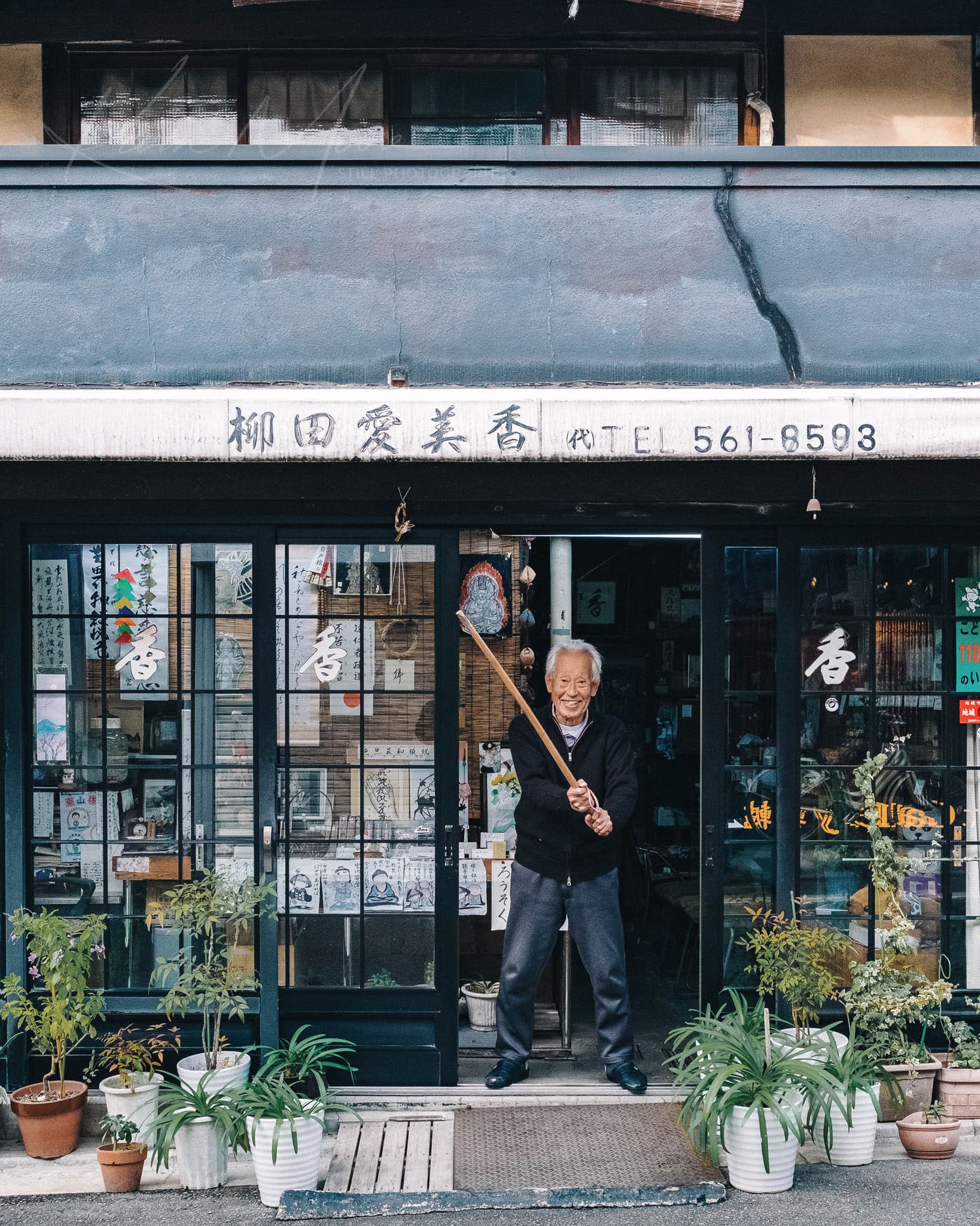 Kyoto antique shop owner tending store, surrounded by traditional architecture and green potted plants.