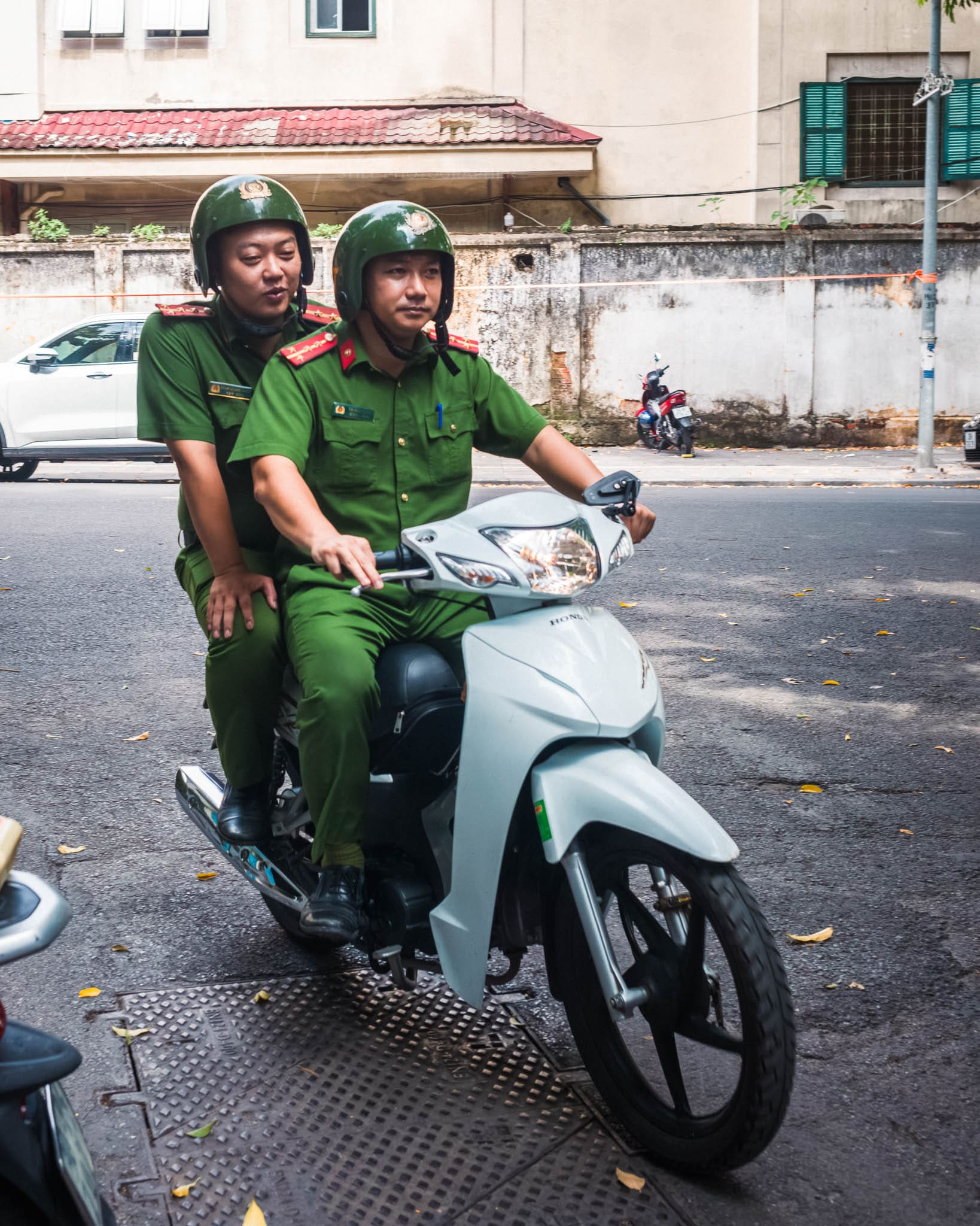 Uniformed individuals riding a modern scooter in an aged urban setting.