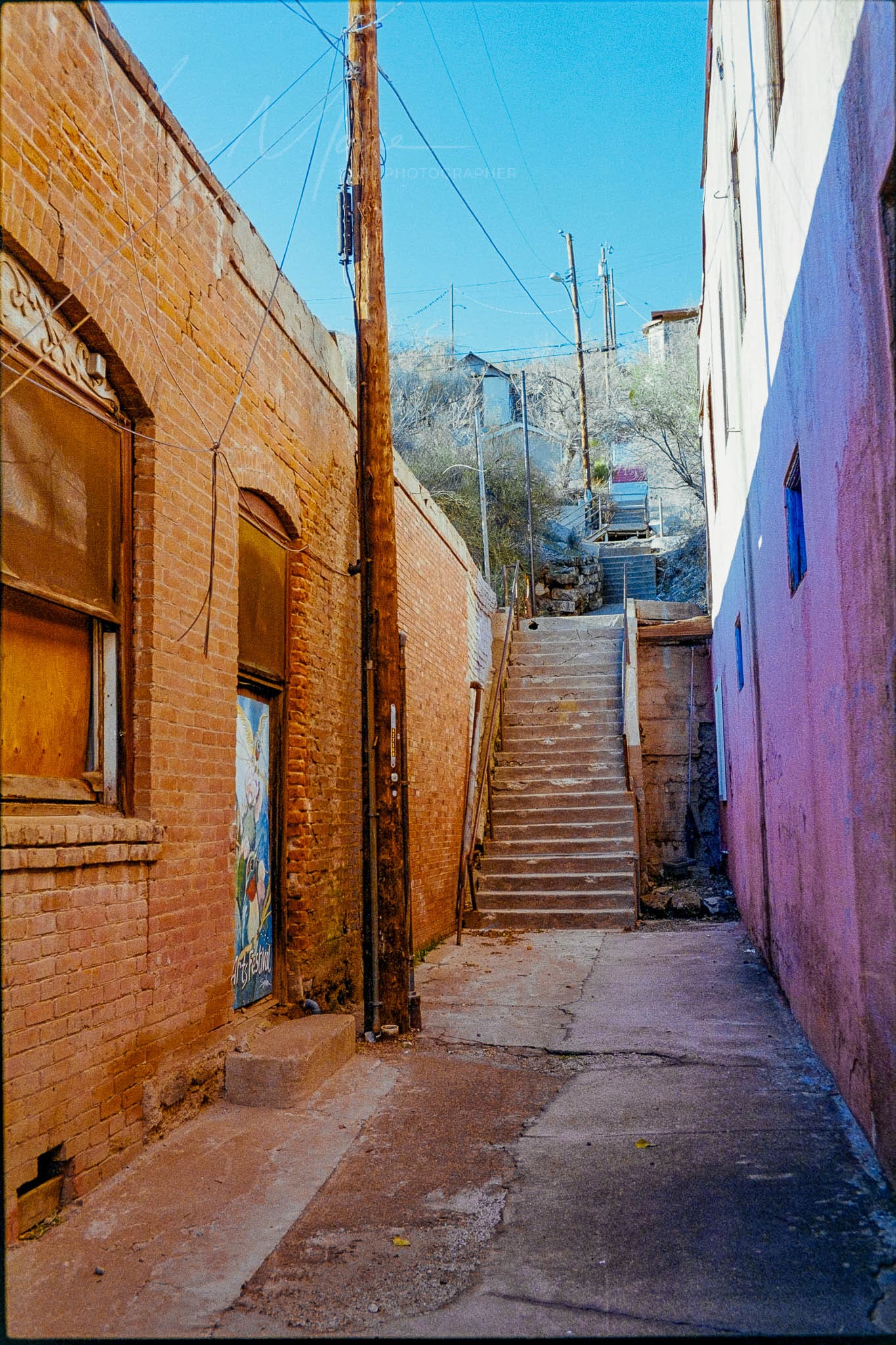 Dimly lit urban alleyway with contrasting buildings leading to a well-worn, sunlit staircase.