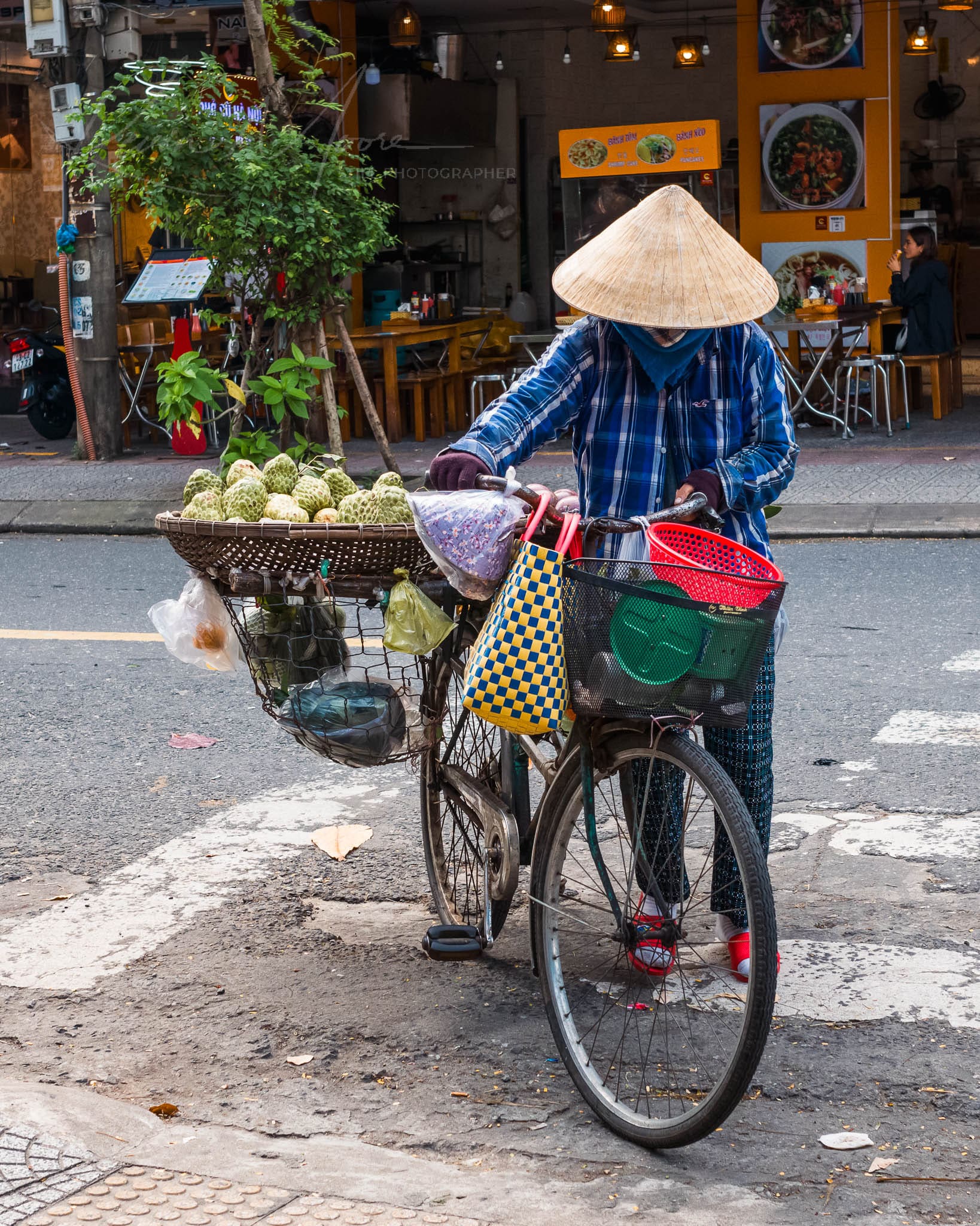 Woman in traditional attire vending goods on a bicycle in a Da Nang city.