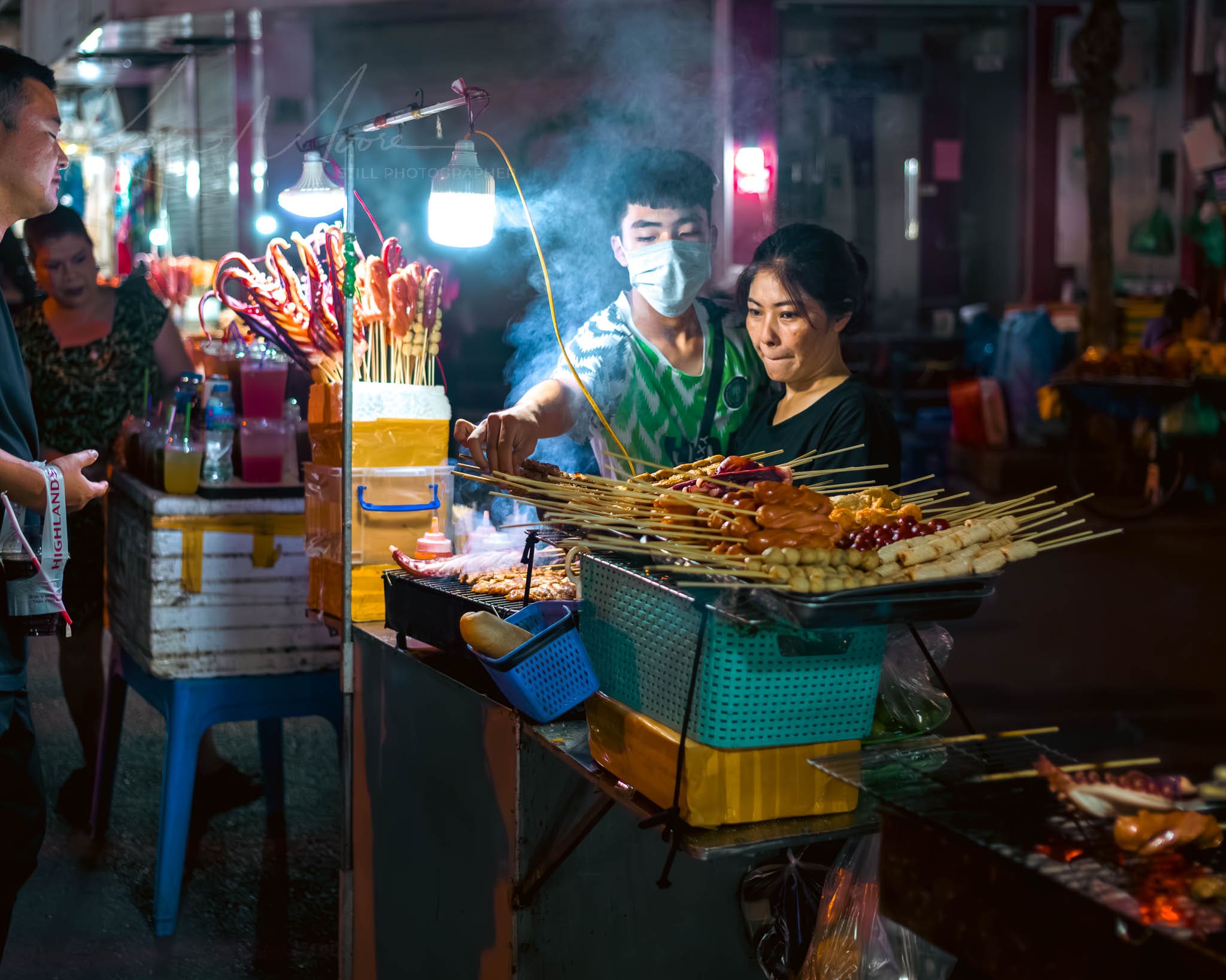 Bustling Hanoi night market food stall with skewered treats and attentive vendors.