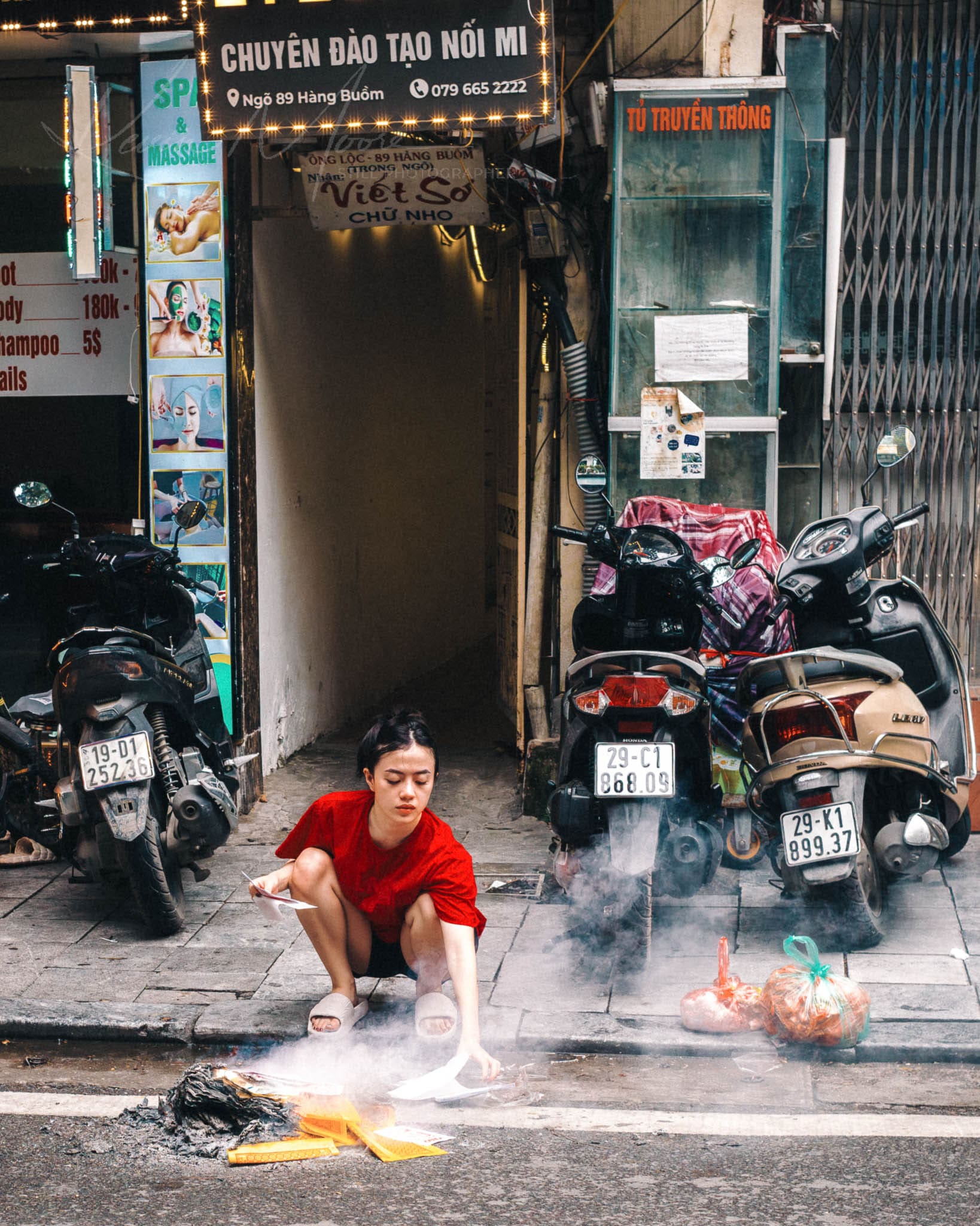 Vietnamese woman performing street ritual with fire amidst urban setting with motorbikes.