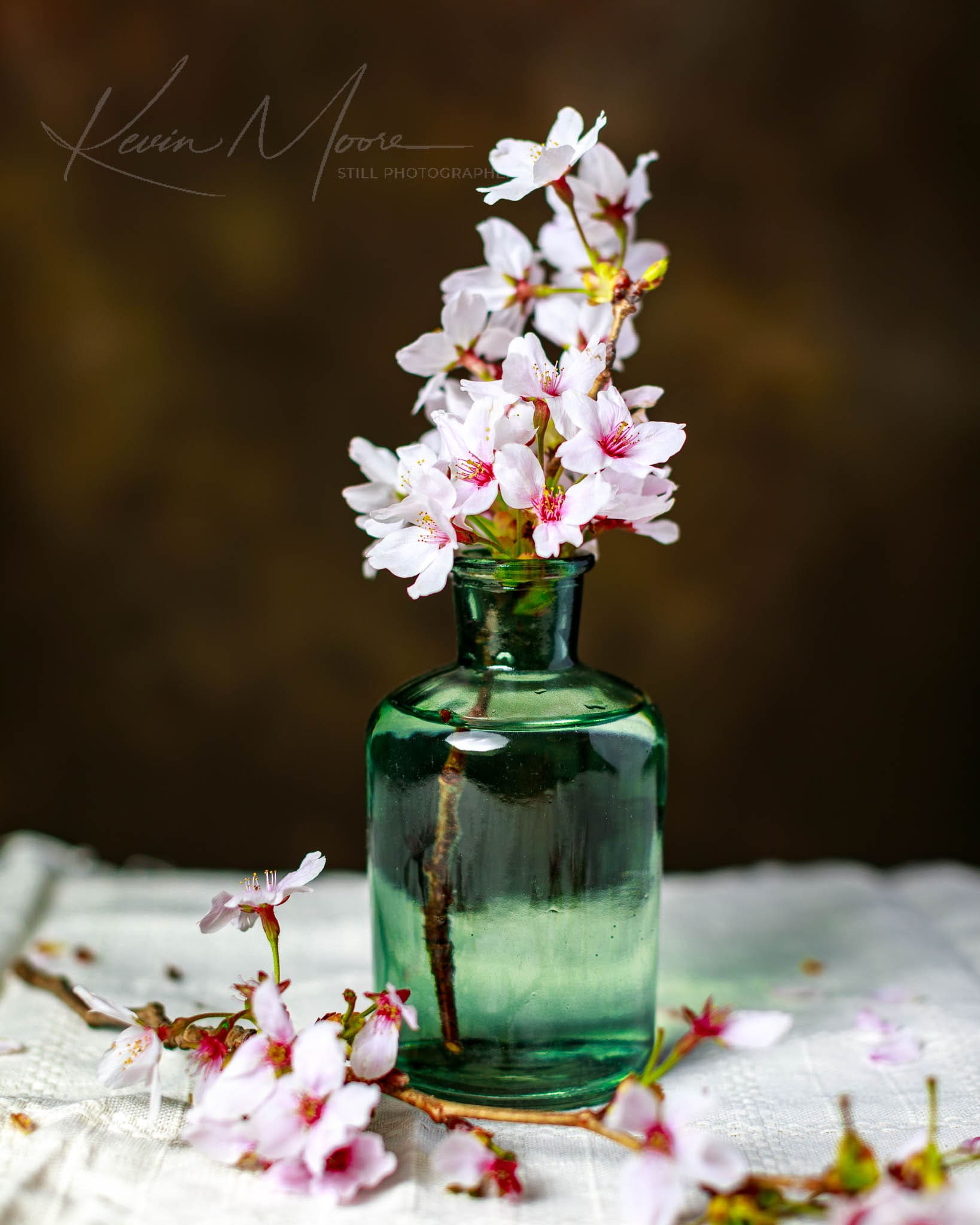 Vintage green glass bottle with delicate cherry blossoms on a white lace backdrop.