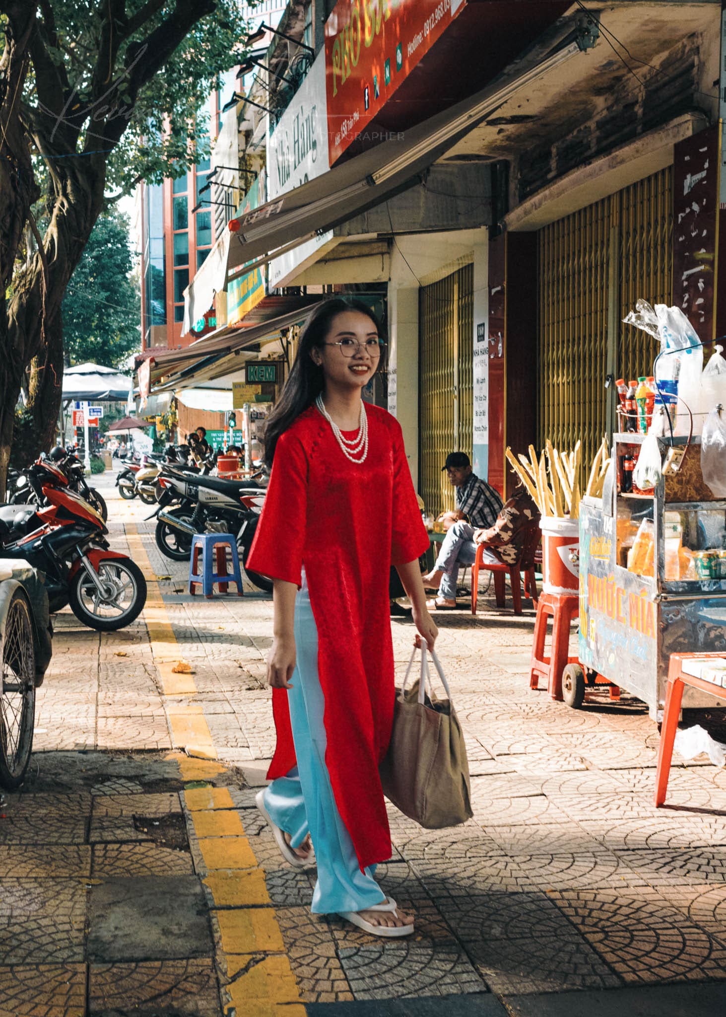 Woman in traditional red attire walking on a bustling Vietnam commercial street.