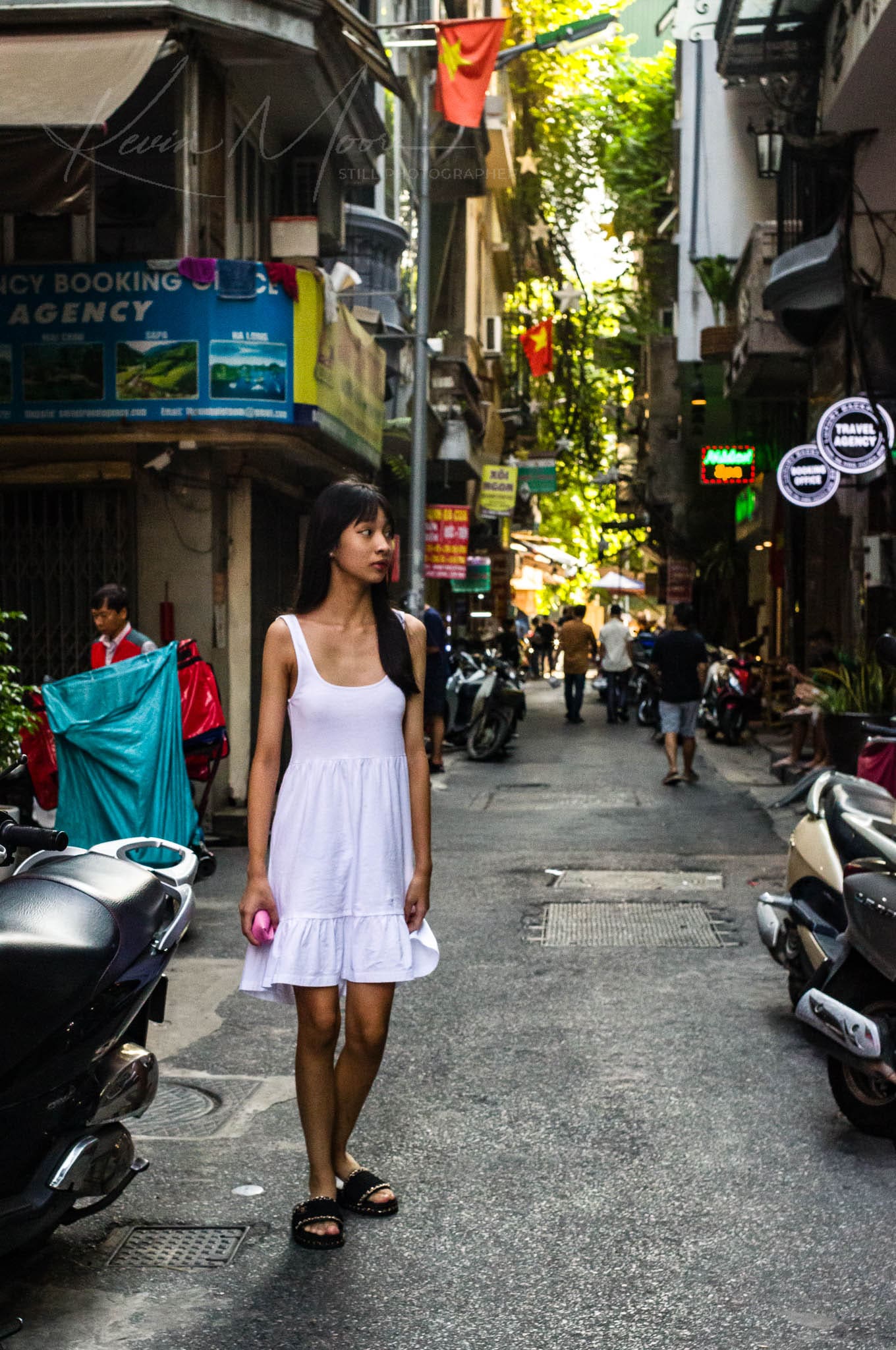 Confident woman in white dress on a bustling Hanoi city street during daytime.