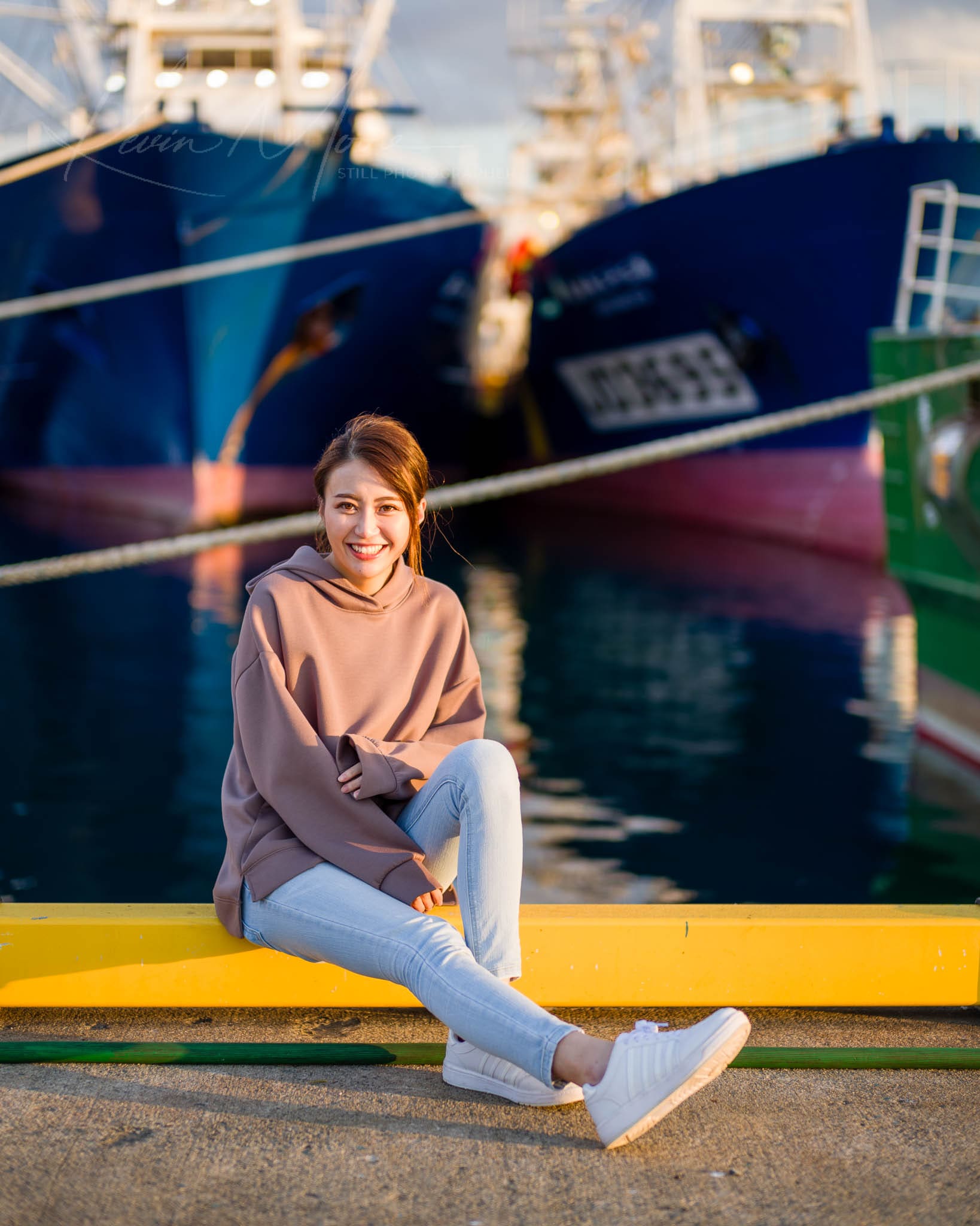 Joyful woman sitting on yellow curb at a boat dock during golden hour.