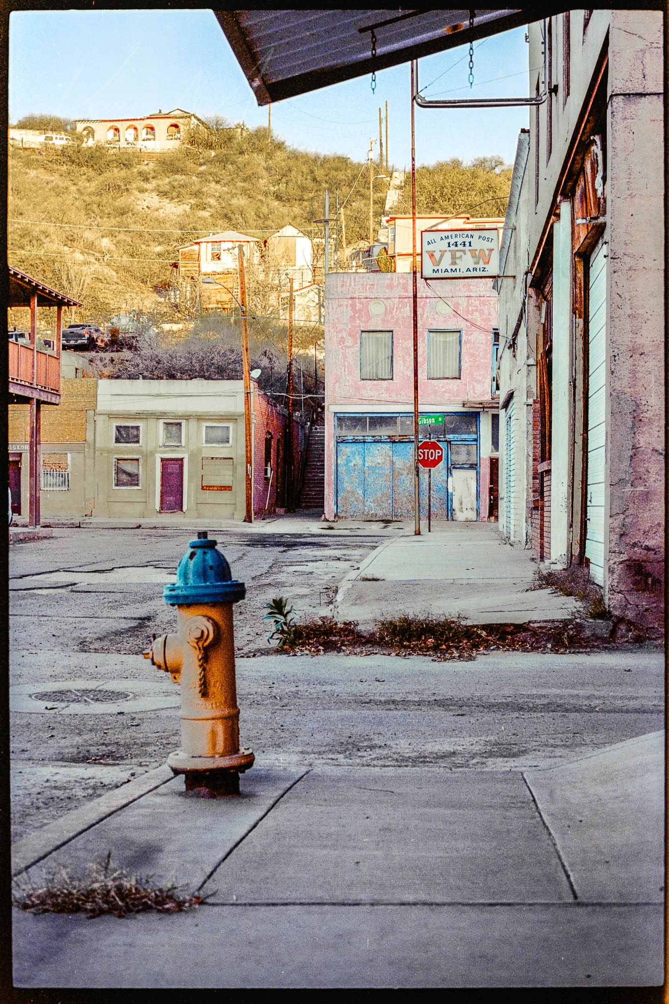 Vibrant fire hydrant standing out in a serene, weathered town nestled in hilly landscape.