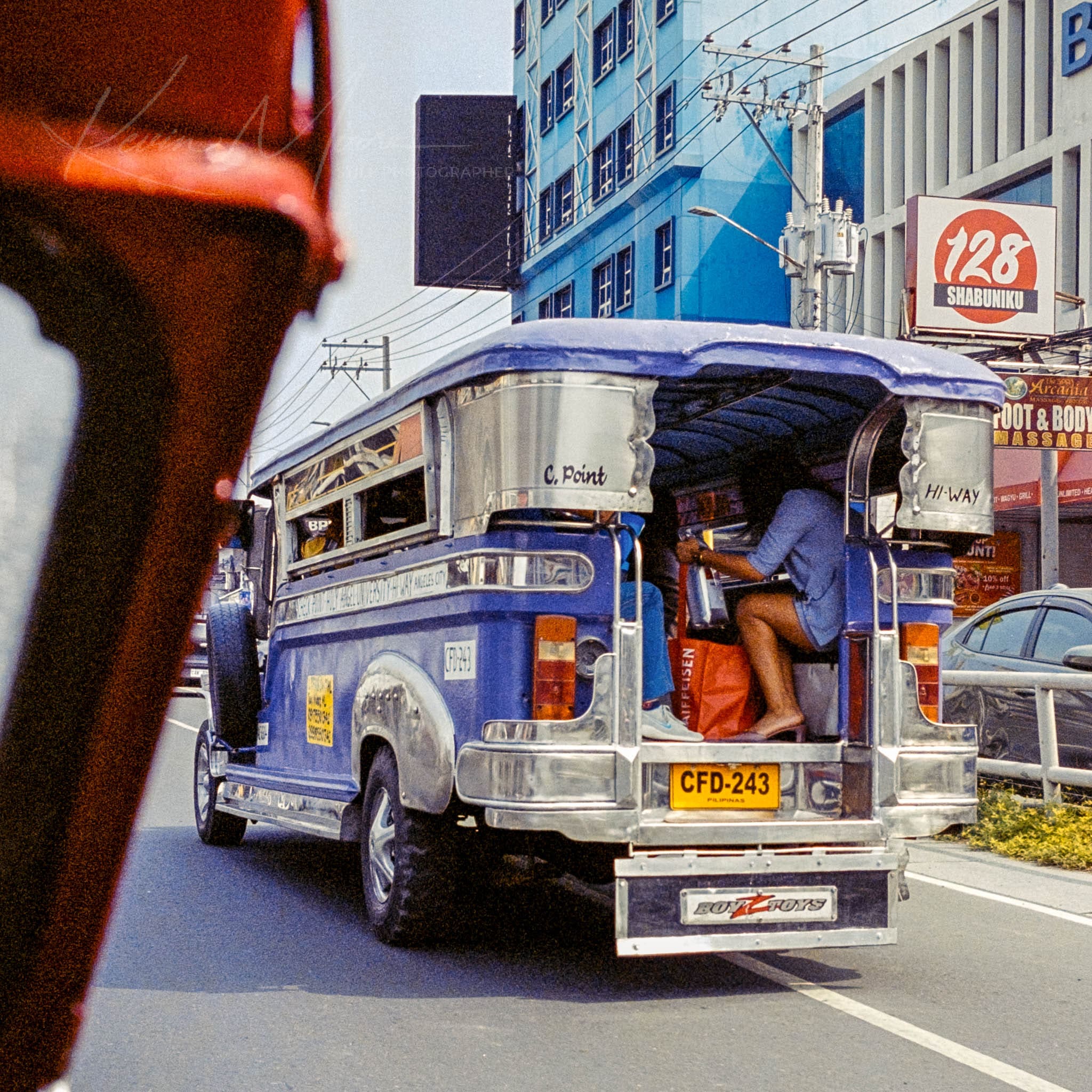 Vibrantly decorated blue jeepney navigating bustling city streets in the Philippines, with visible passenger.