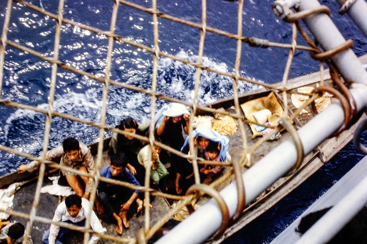 Group of boat people refugees viewed through a net while navigating in a small wooden boat on wavy sea.