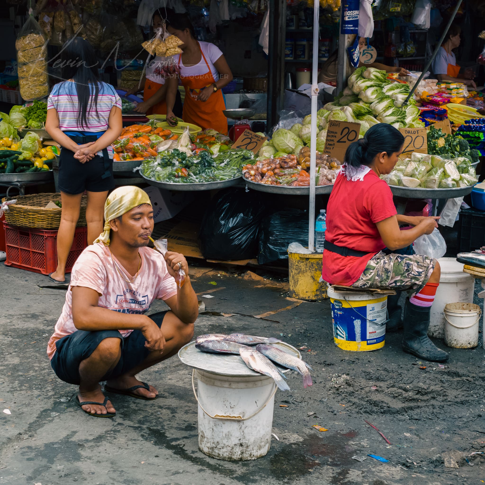 Man selling fresh fish amidst vibrant produce at a busy local market.