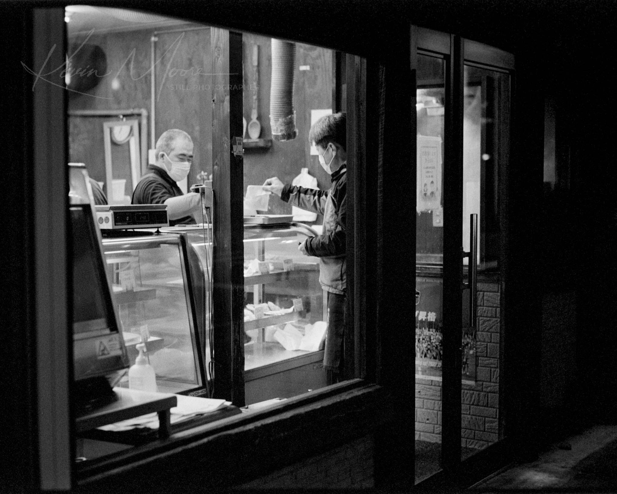 Black-and-white image of a timeless, friendly exchange in a local nighttime shop.