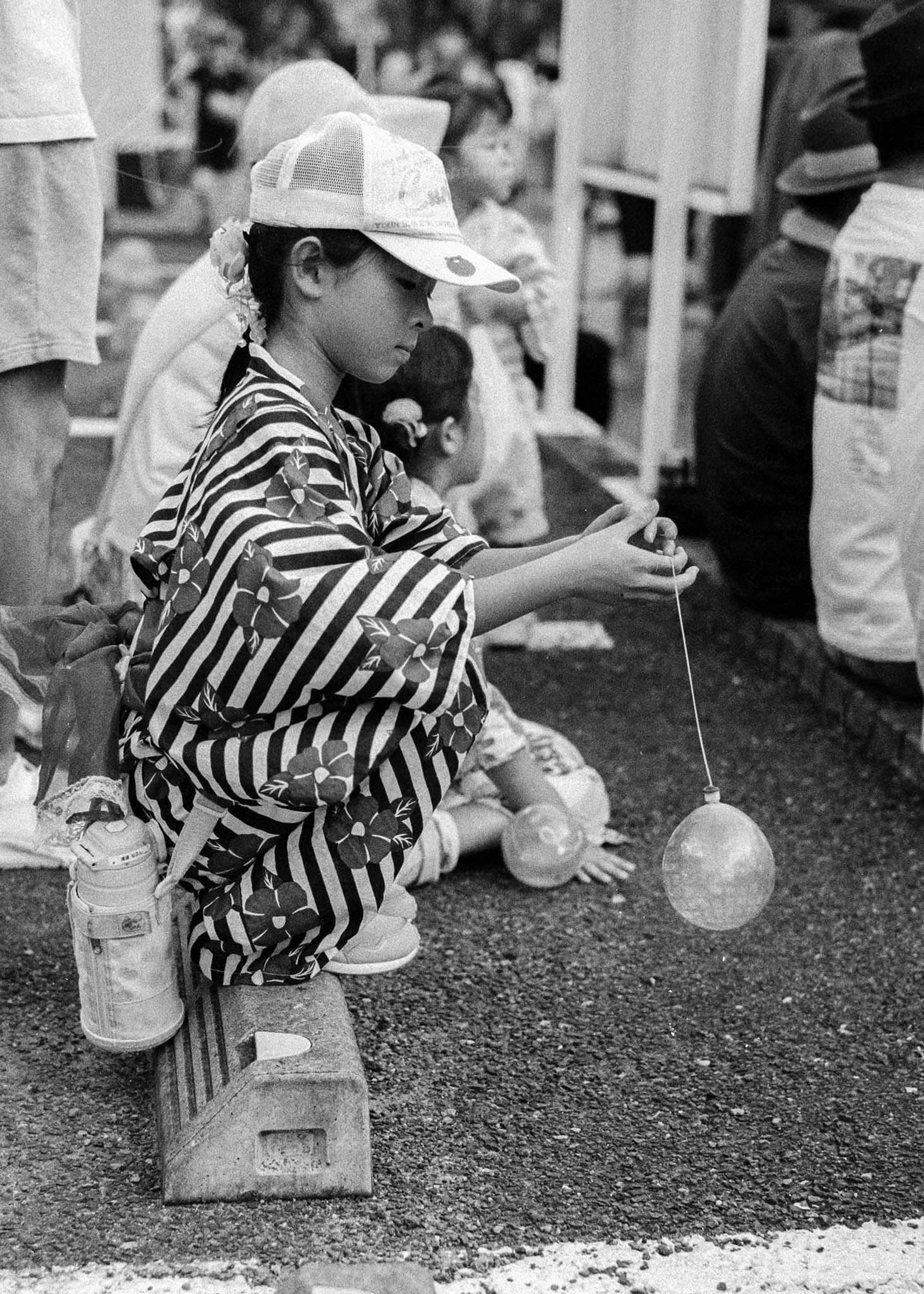 Japanese child intently playing a traditional outdoor game, balancing water-filled balloon.