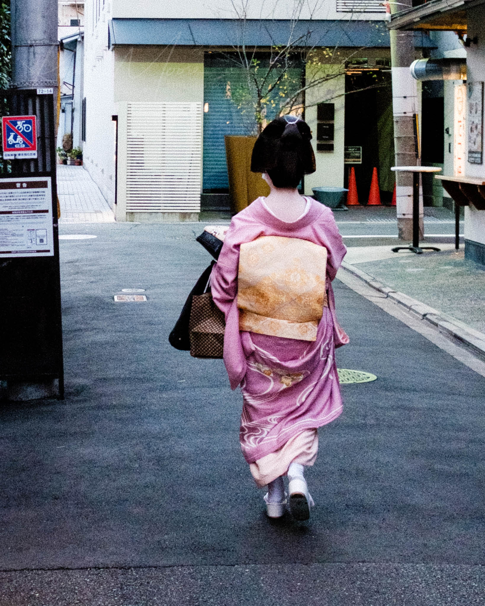 Geisha in vibrant pink kimono navigating modern urban Japanese street