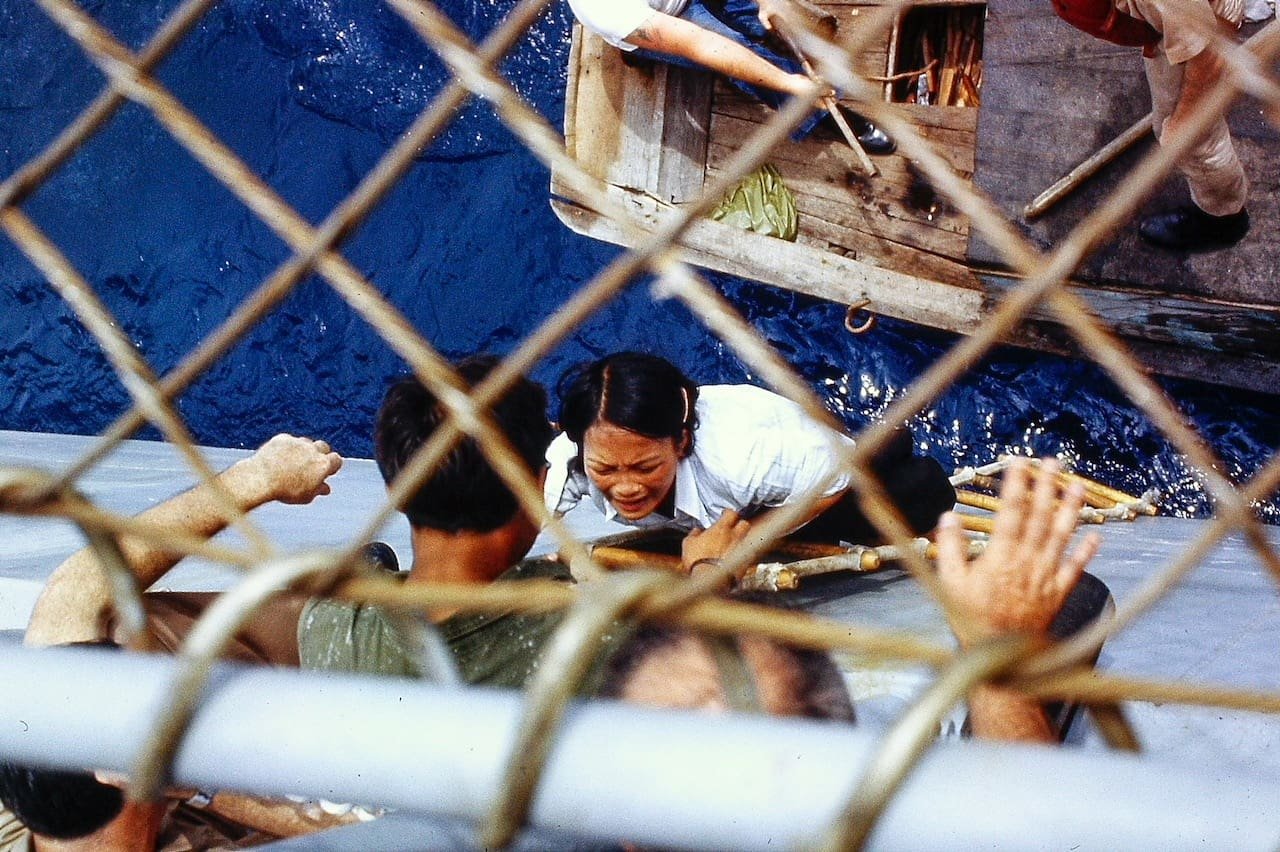 Dramatic rescue scene of woman in boat viewed through wire mesh fence.