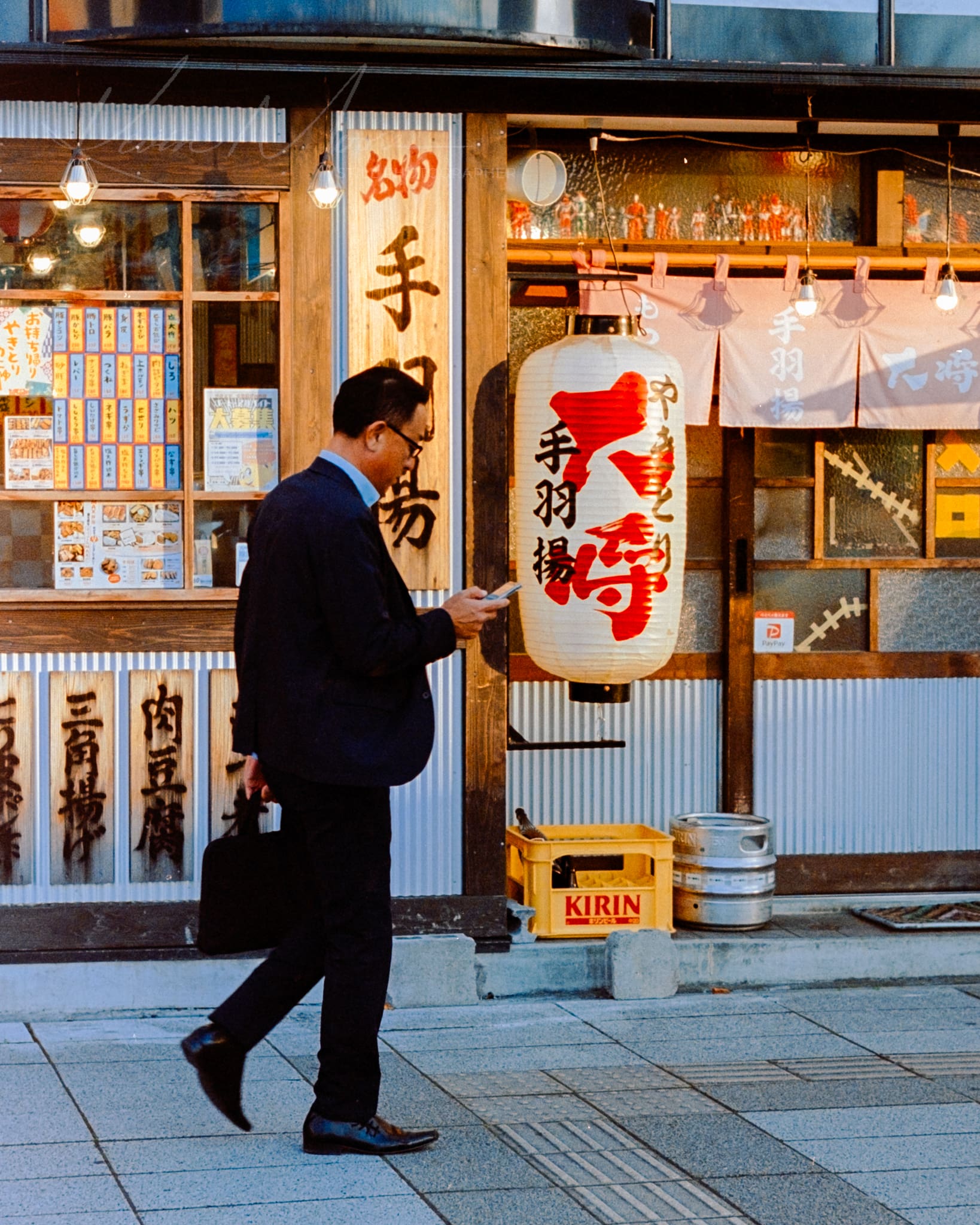 Businessman passing by a traditional Japanese restaurant at dusk in urban cityscape.