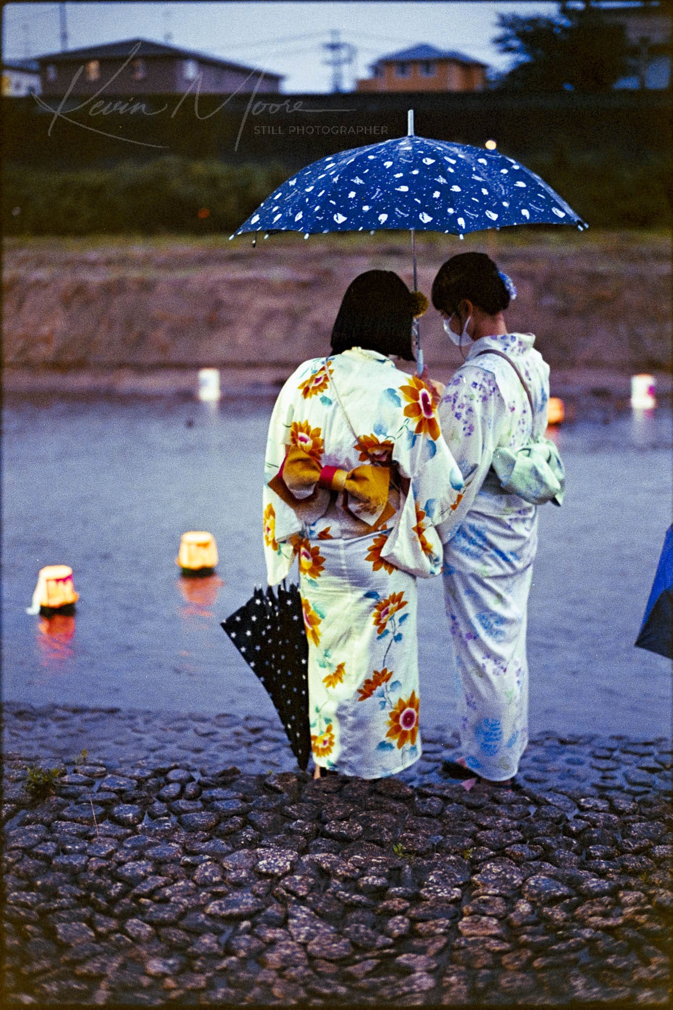Two young women in kimonos participating in a Japanese lantern ceremony by the water