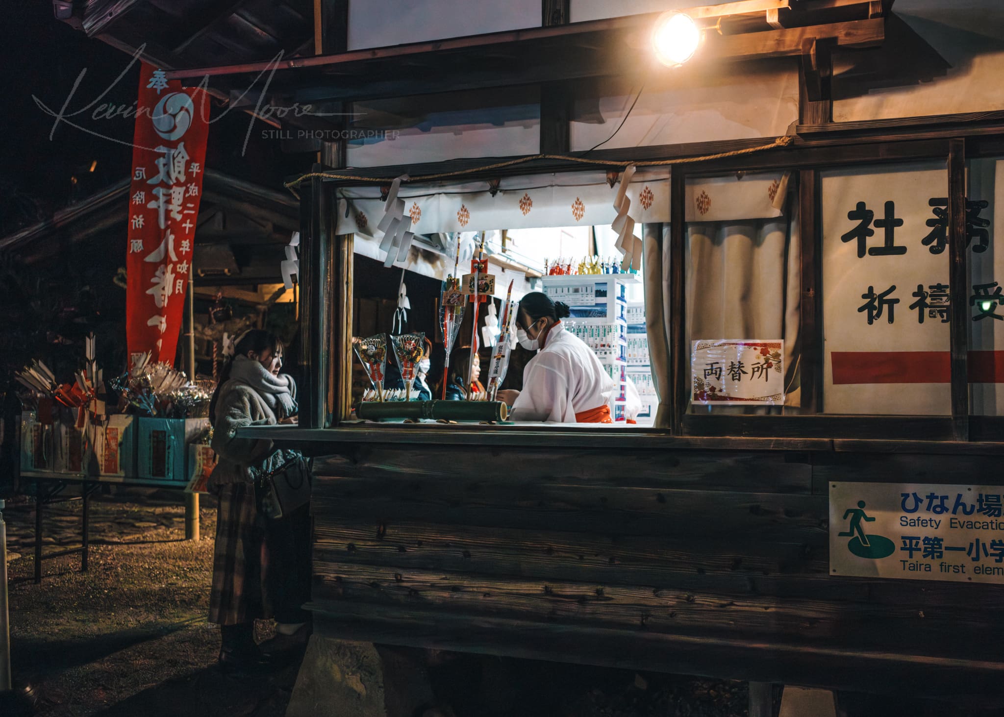 Woman at a traditional Japanese shrine at night buying religious souvenirs.