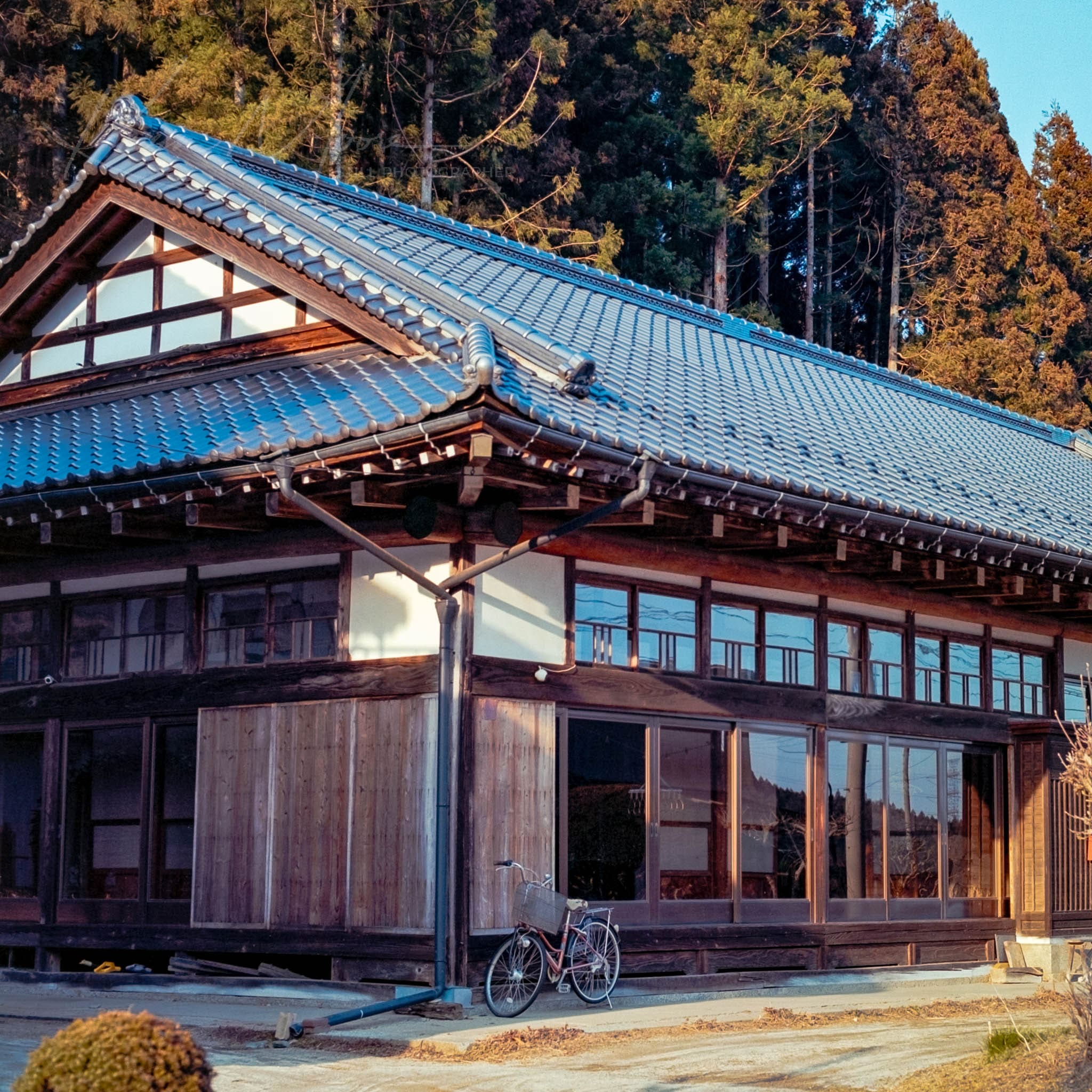 Traditional Japanese home at dusk, featuring rustic woodwork, large windows, and a solitary parked bicycle.