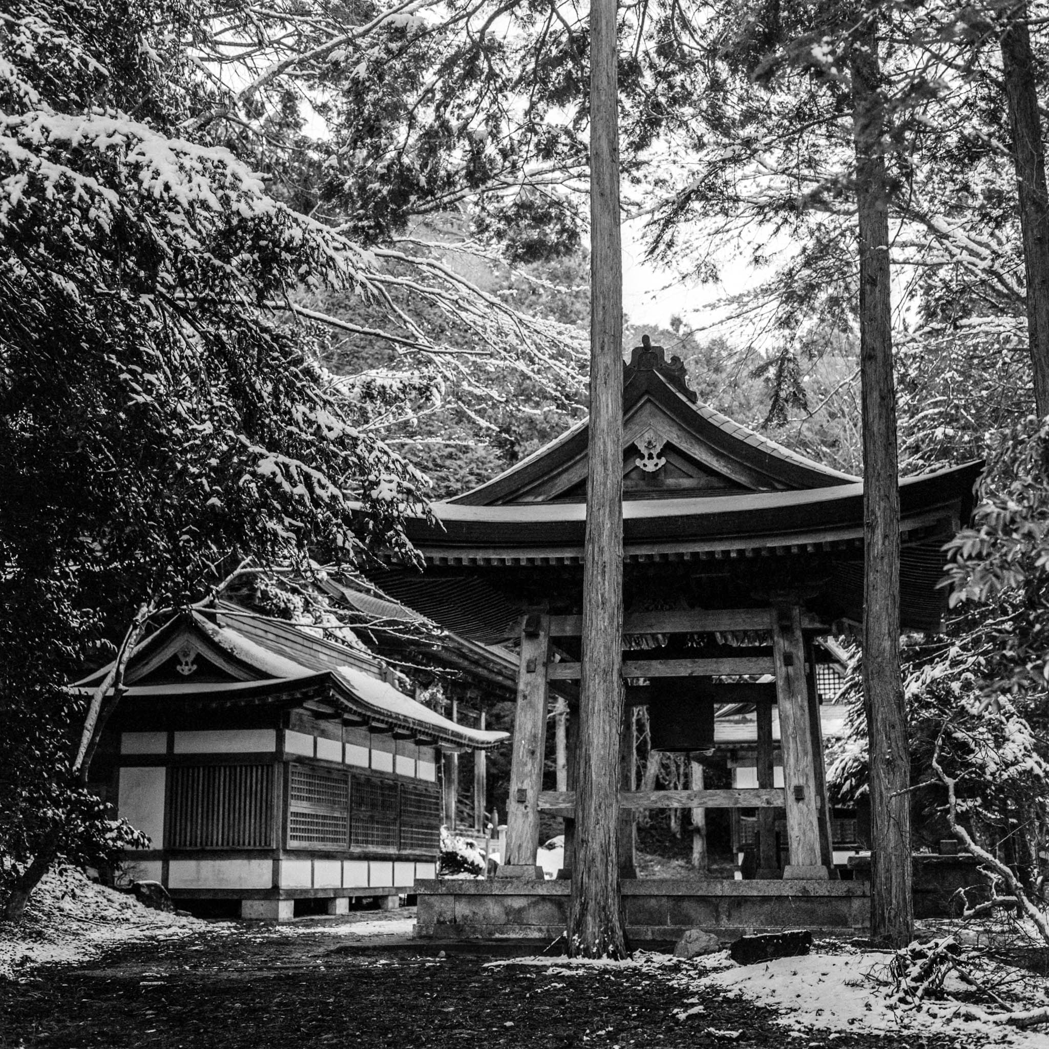 Winter view of a secluded Japanese temple amidst snowy forest in black and white photograph.