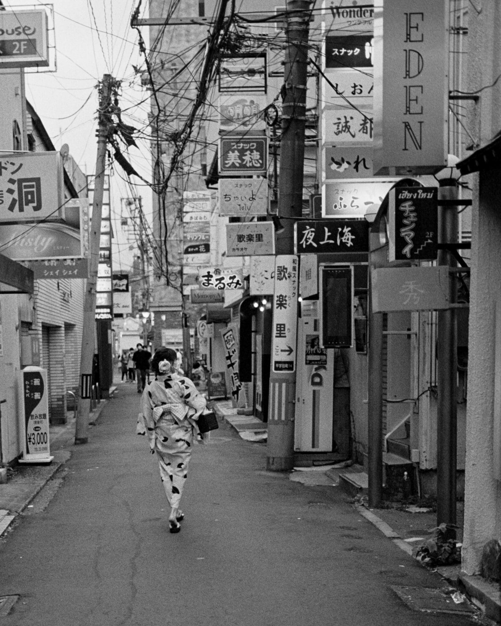 Kimono-clad person in a bustling Japanese alley, a contrast of tradition and modernity in monochrome.